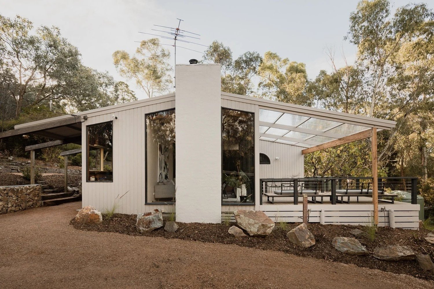Mid-Century House: a white gabled house with a chimney and a wall of glass among gum trees