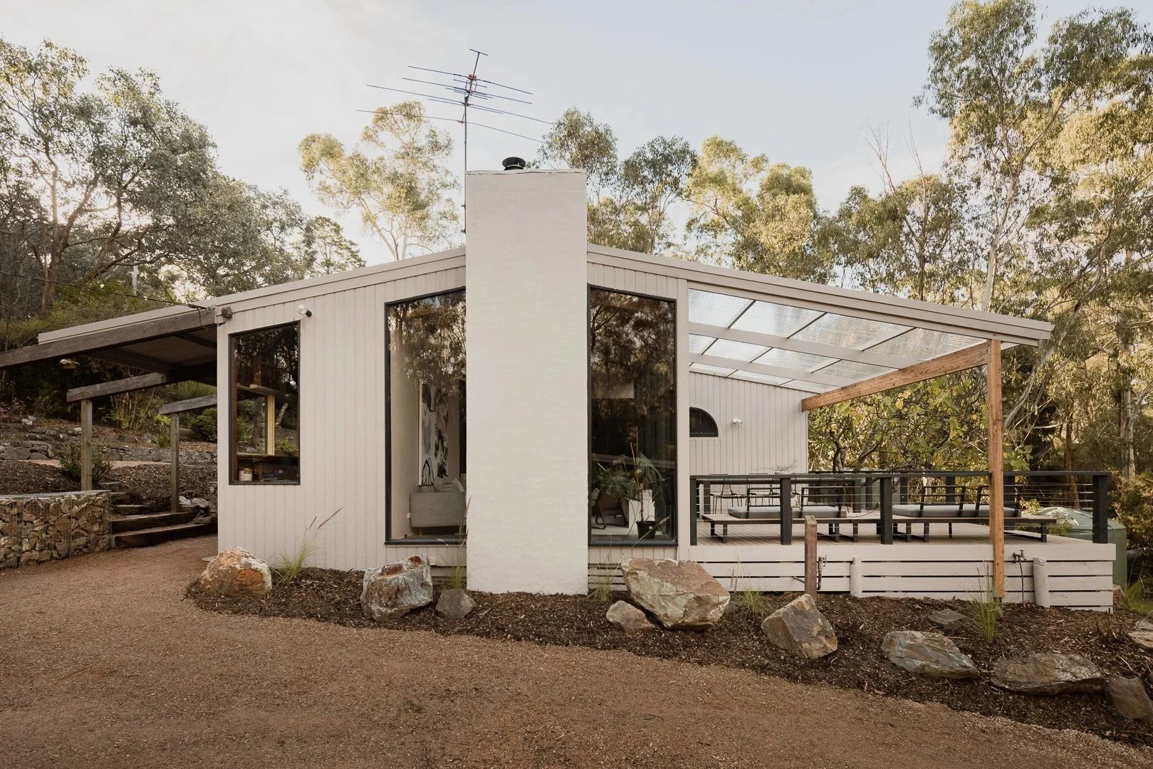 Mid-Century House: a white gabled house with a tall chimney and a wall of black-framed glass, set among gum trees