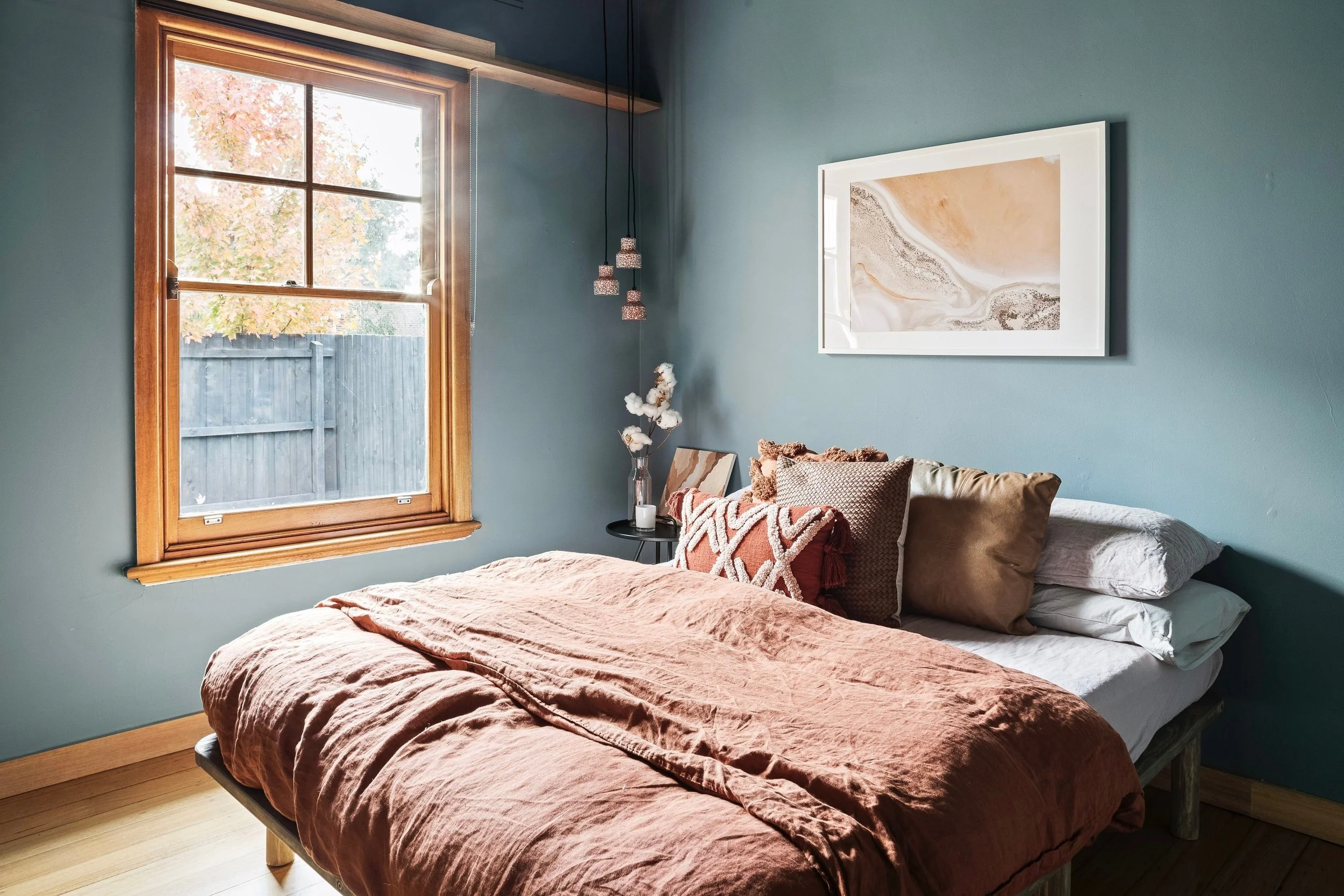 Bedroom with rust linen bedding, a coastal artwork and a timber-framed window