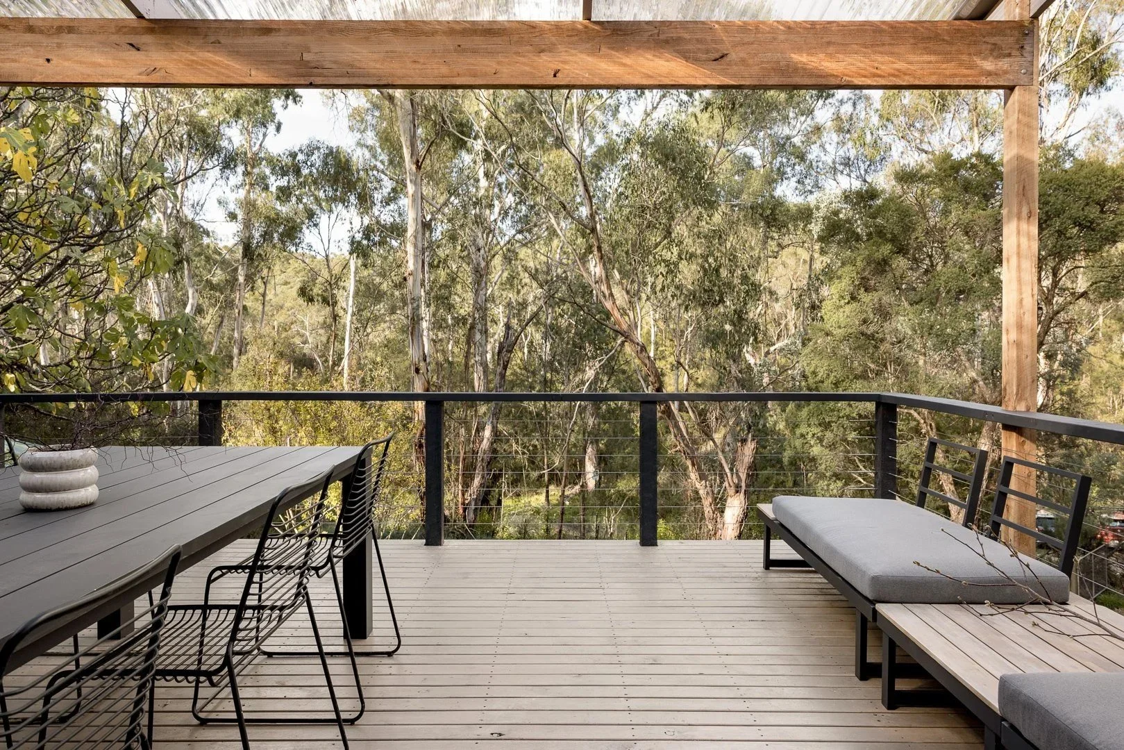 Covered deck with an outdoor dining table and built-in bench, looking out to the bush