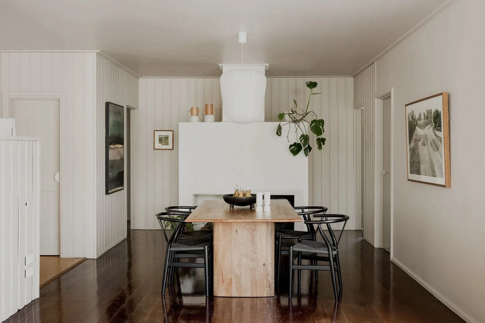 Dining table with black chairs in front of the white fireplace and vertical board walls