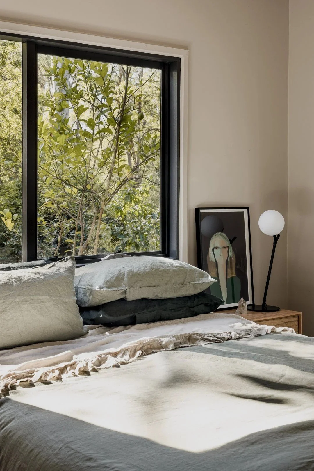 Bedroom with layered linen bedding beside a black-framed window to the trees