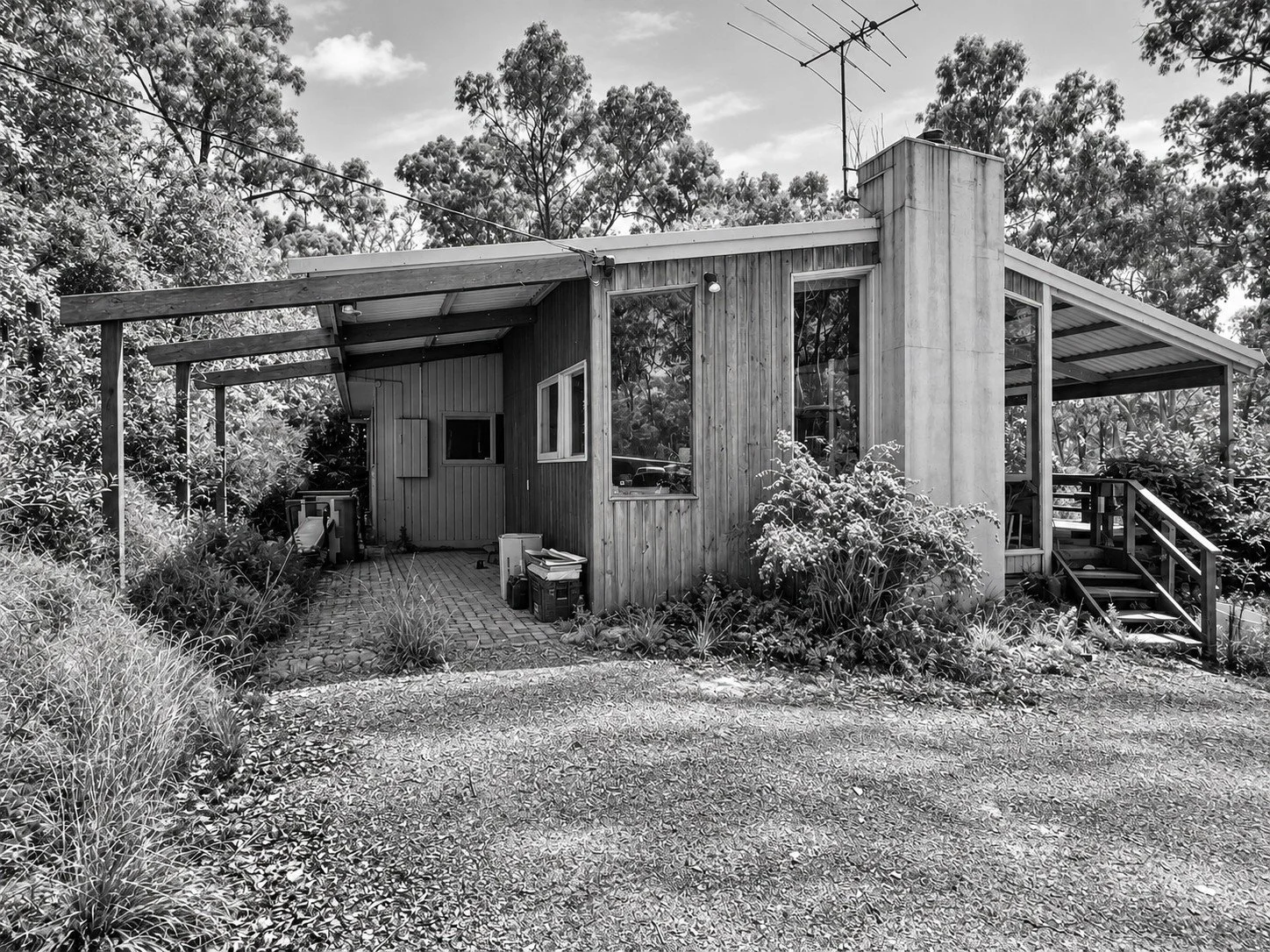 Before: the front of the house with weathered vertical timber boards, the chimney and the covered outdoor room