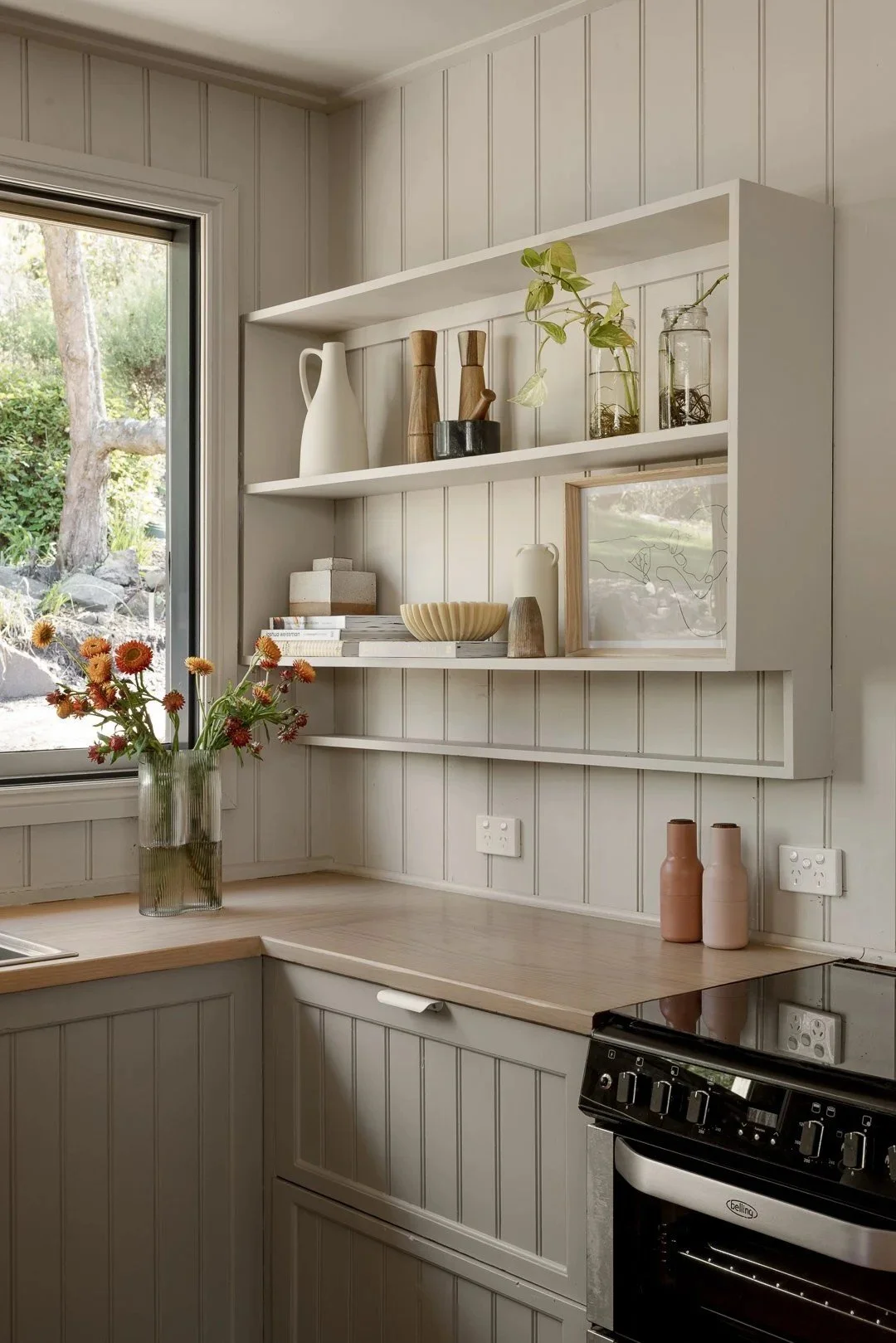 Open timber shelves with ceramics beside the kitchen window