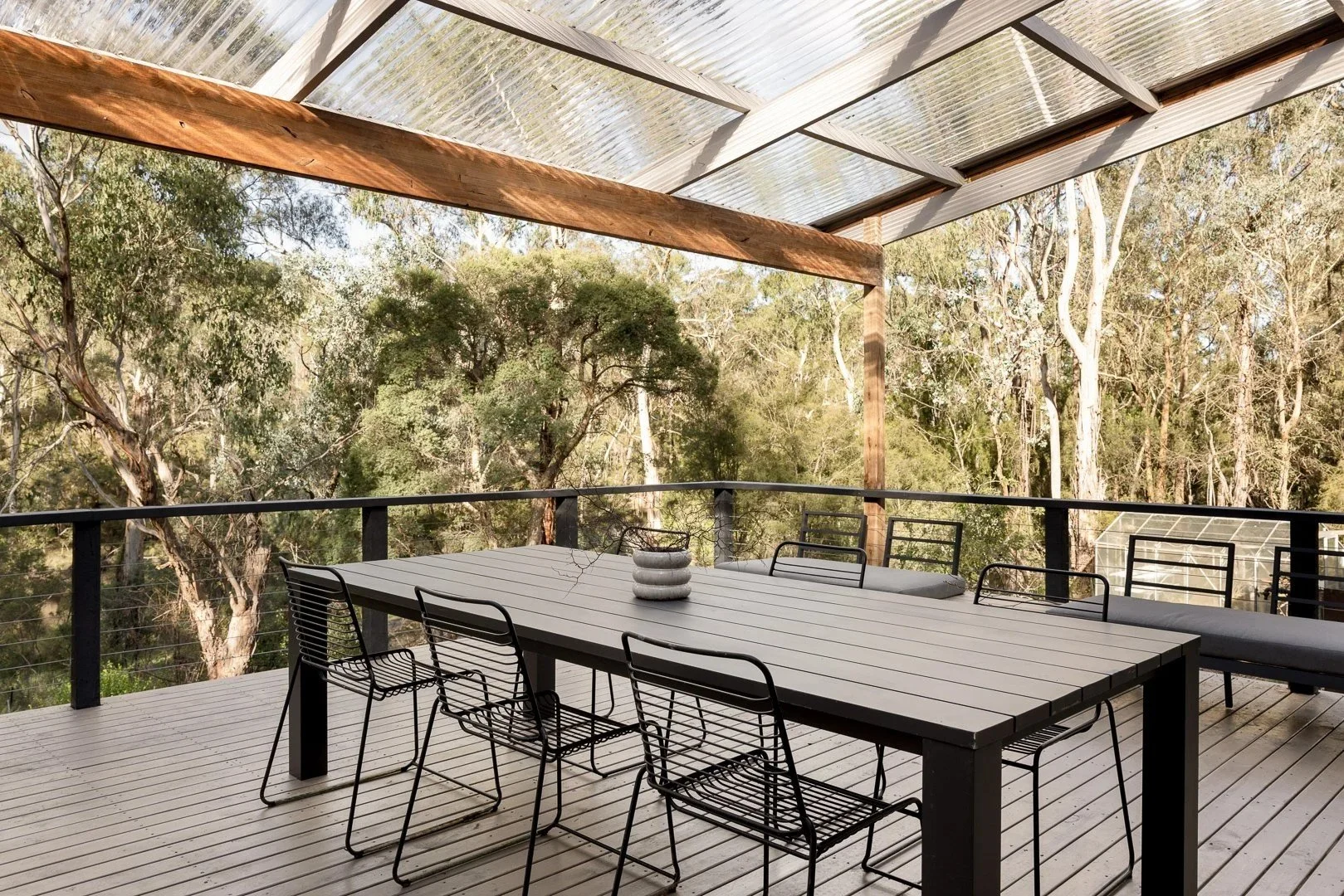 Outdoor dining table under a translucent roof, with the bush beyond