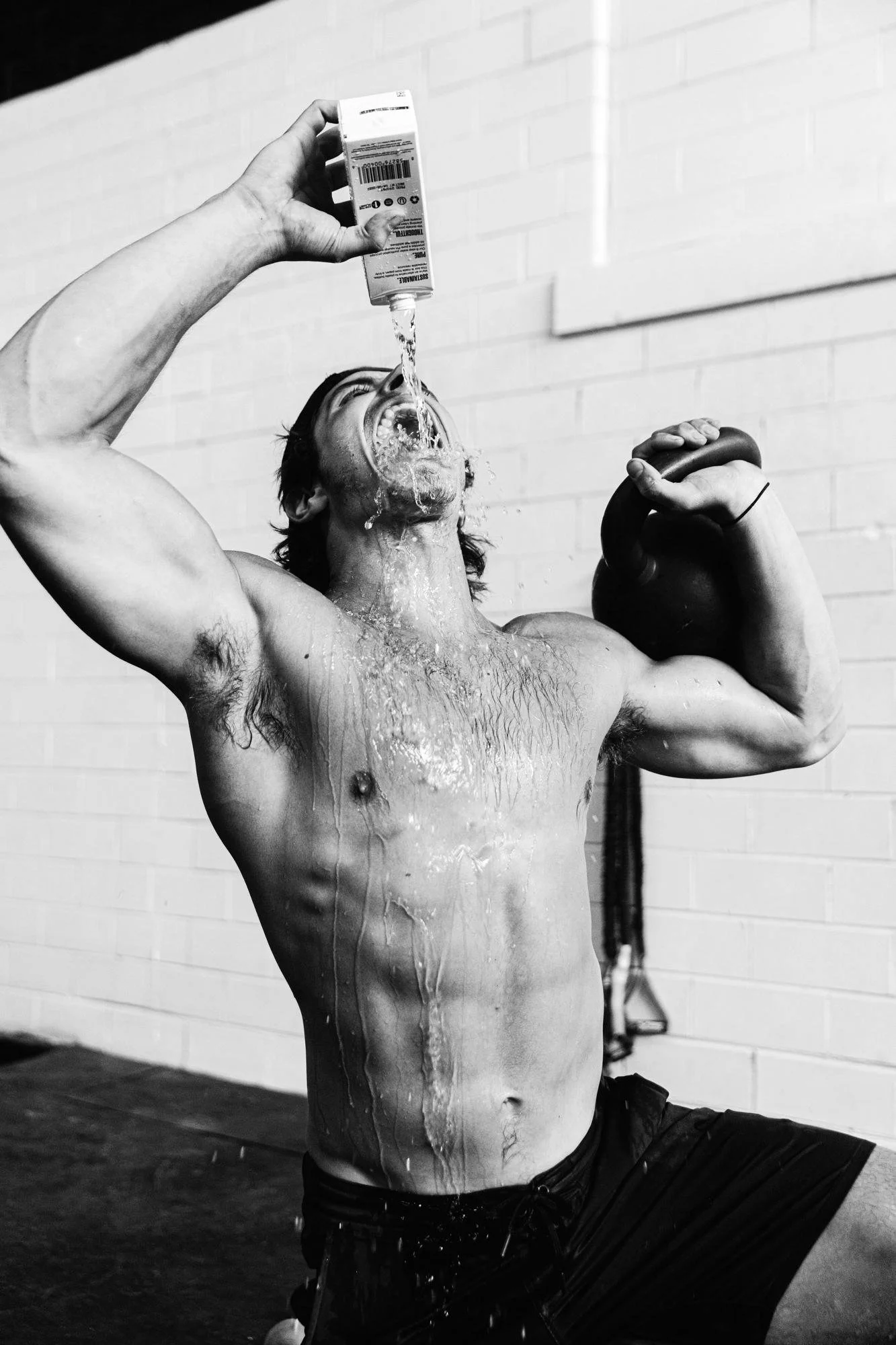 A shirtless athlete pouring water over himself after a workout