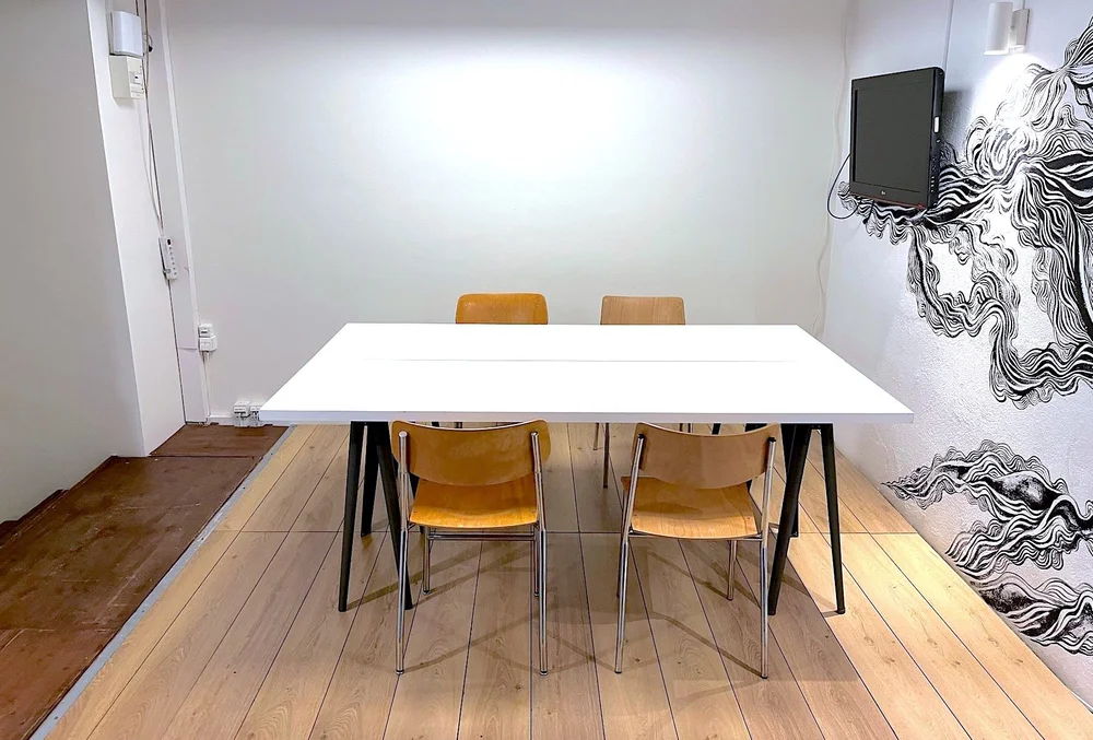 Betty Room in a 2-person setup, with a white table and screen, available for rent in Geneva