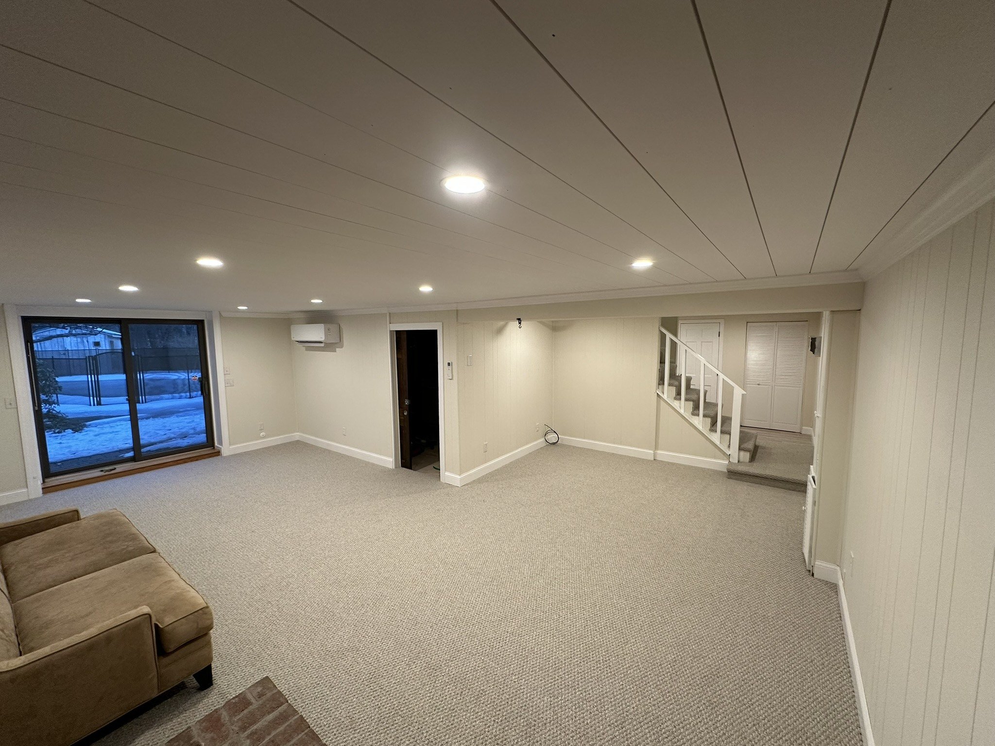 Finished carpeted basement room viewed toward the sliding door and stairs