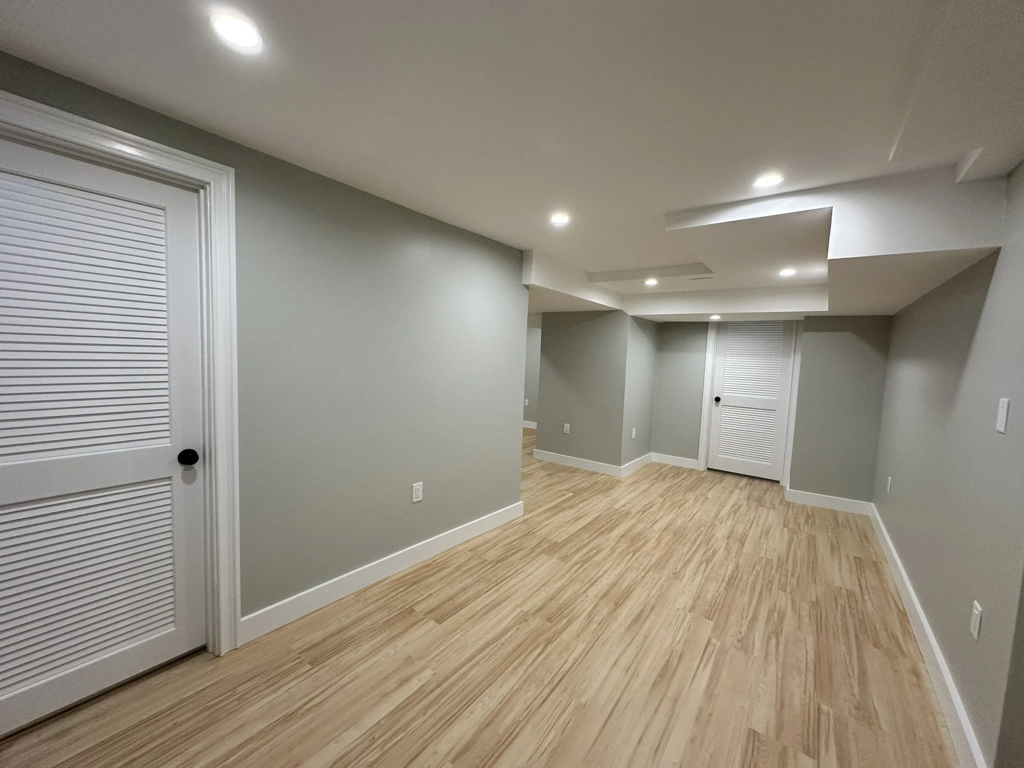 Finished basement with gray walls, white doors and plank flooring