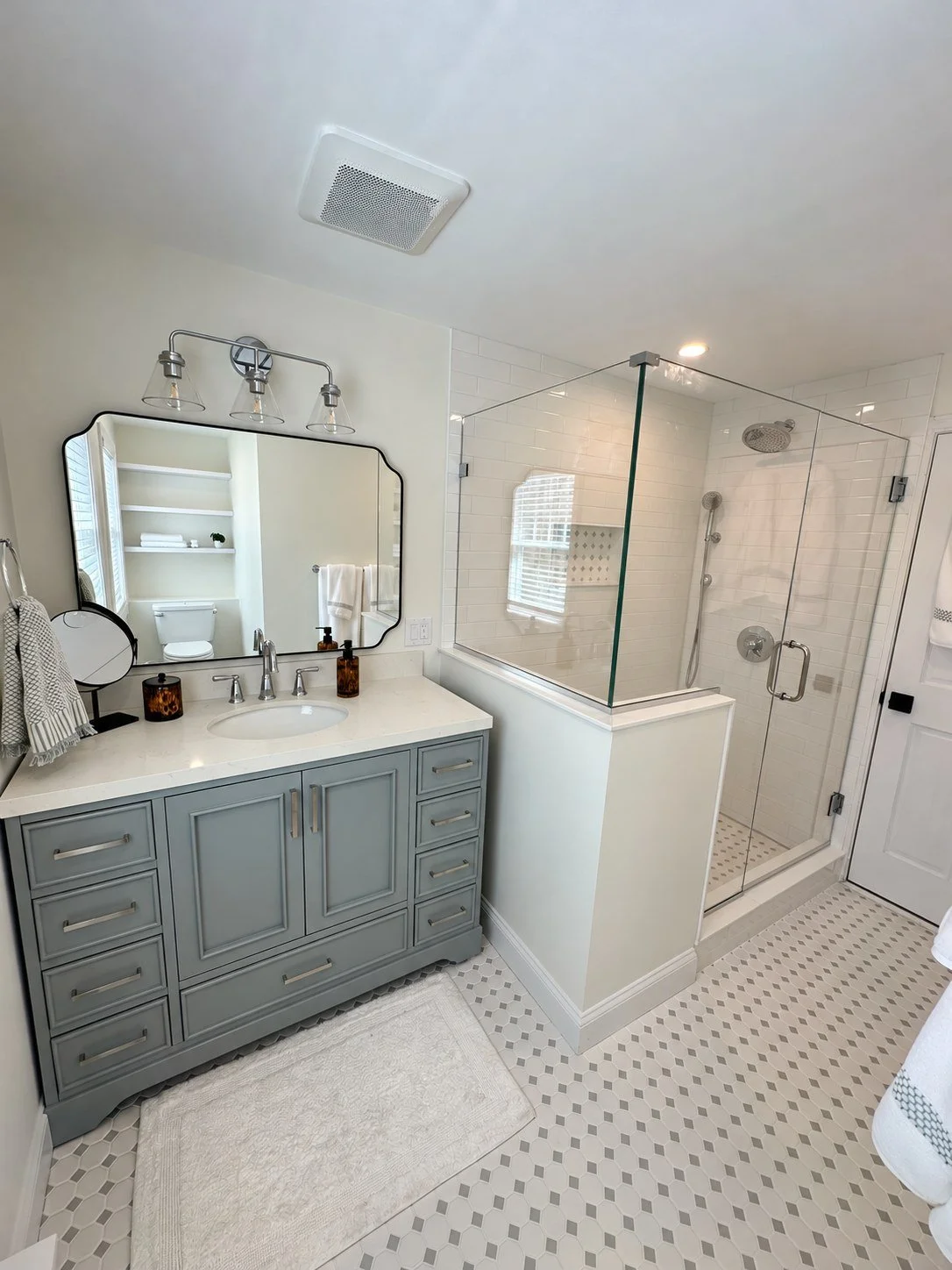 Remodeled bathroom with gray vanity, installed glass shower enclosure and patterned tile floor