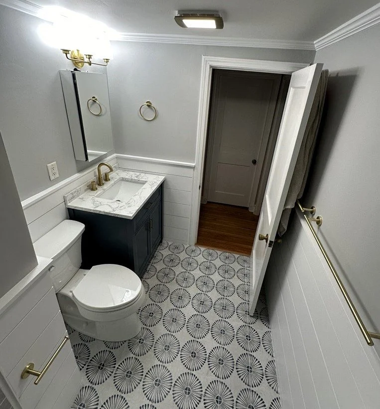 Bathroom with patterned tile floor, shiplap wall trim, dark vanity and brass hardware