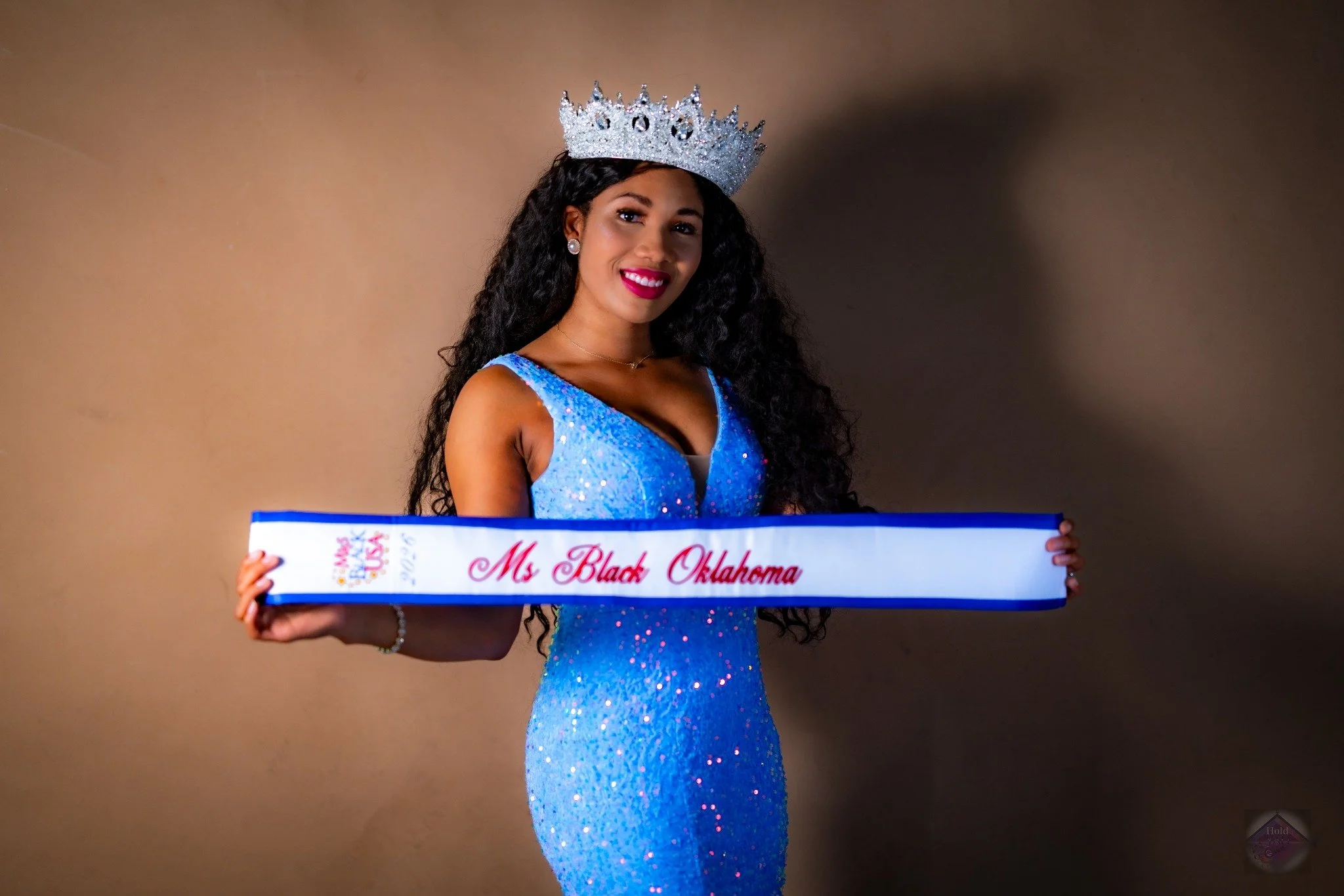 Fashion portrait of a crowned woman wearing a blue sash by HOLD YAH OWN