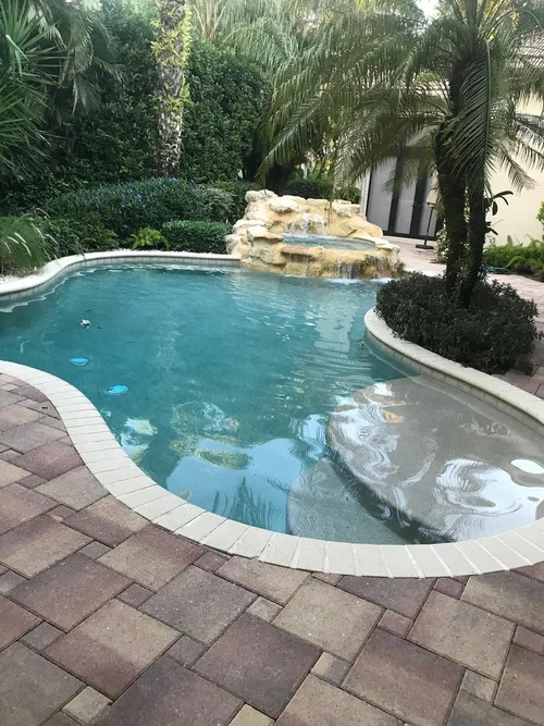 Refilled curved pool with a rock waterfall following resurfacing in BallenIsles.
