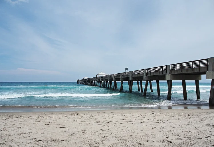 Juno Beach Pier extending over turquoise Atlantic waves beside the sandy beach.