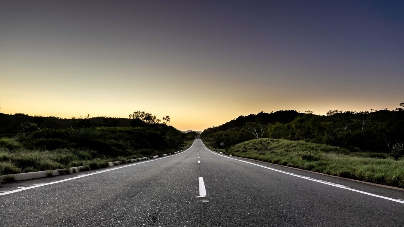 A tranquil road stretches into the distance, flanked by greenery under a sky showing the gradient of dusk to night, embodying calmness and continuity.