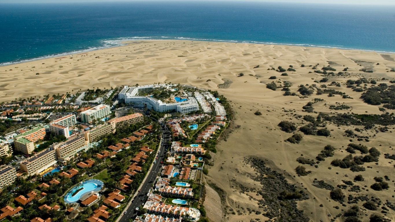 Aerial view of a coastal resort area in Gran Canaria, with expansive sand dunes meeting the calm ocean, highlighting the region’s popular vacation spots.