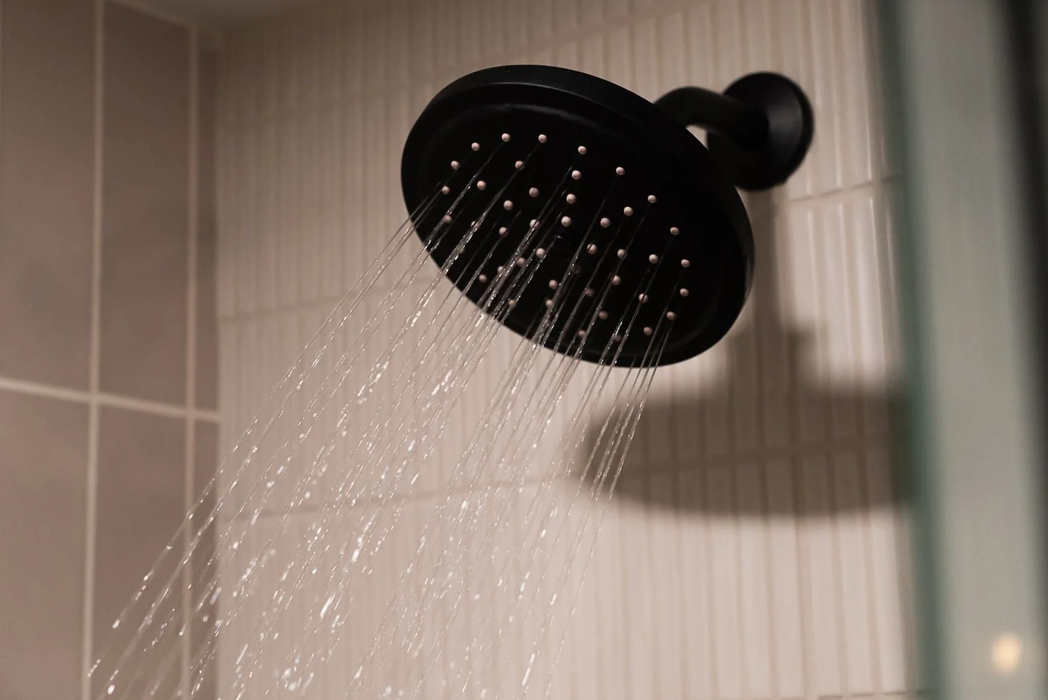 Matte black rain shower head in a tiled step-in shower
