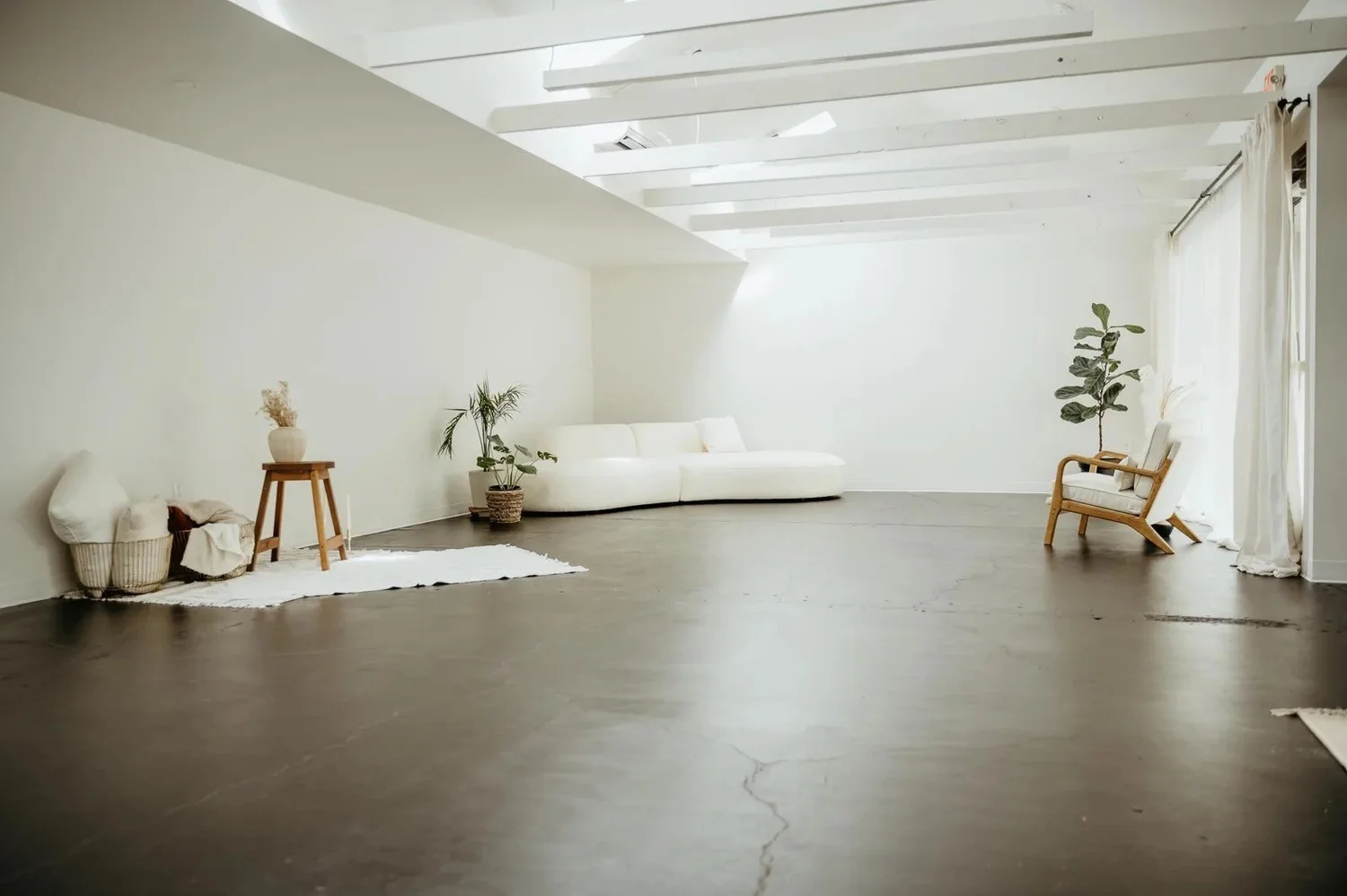 Suite 120 staged as a bright studio, with white beams, a curved sofa and sheer curtains along the glass