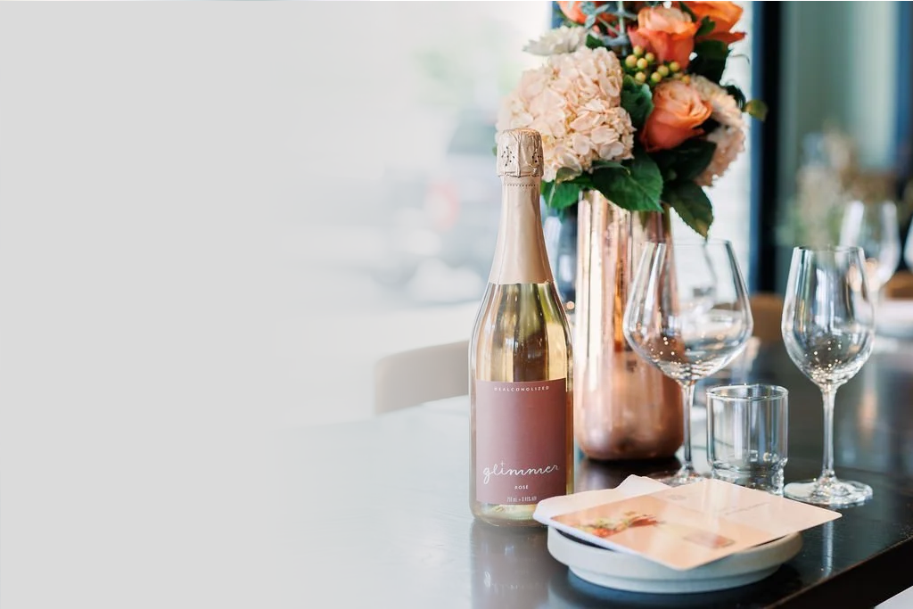A table set for celebration with a bottle of Glimmer sparkling wine, glasses, and flowers