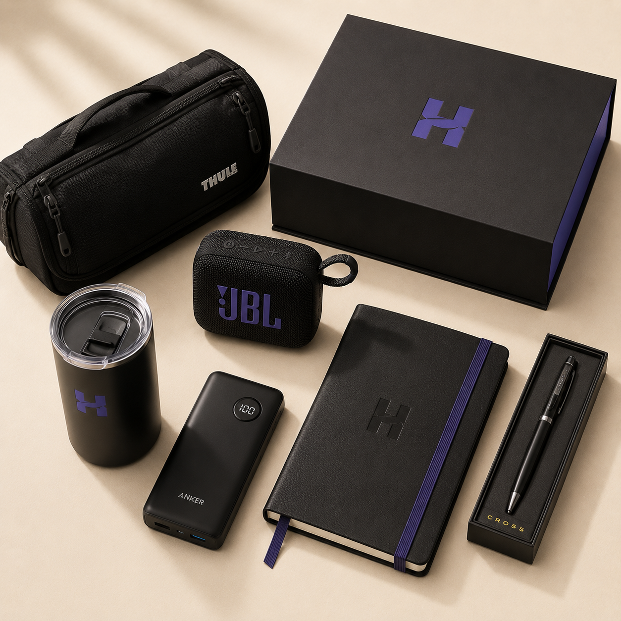 Premium corporate gift collection featuring a Thule travel organizer, JBL speaker, Anker power bank, Cross pen, insulated tumbler, and executive gift box arranged in an editorial flat lay.
