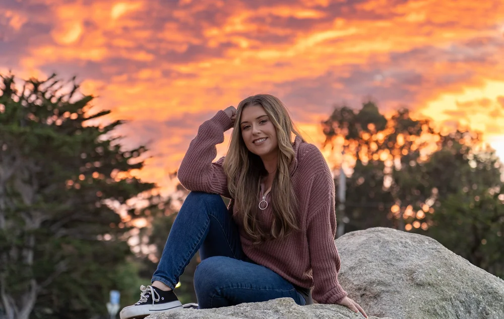 Kaila Kraft, author of Am I Changed?, sitting on a rock at sunset