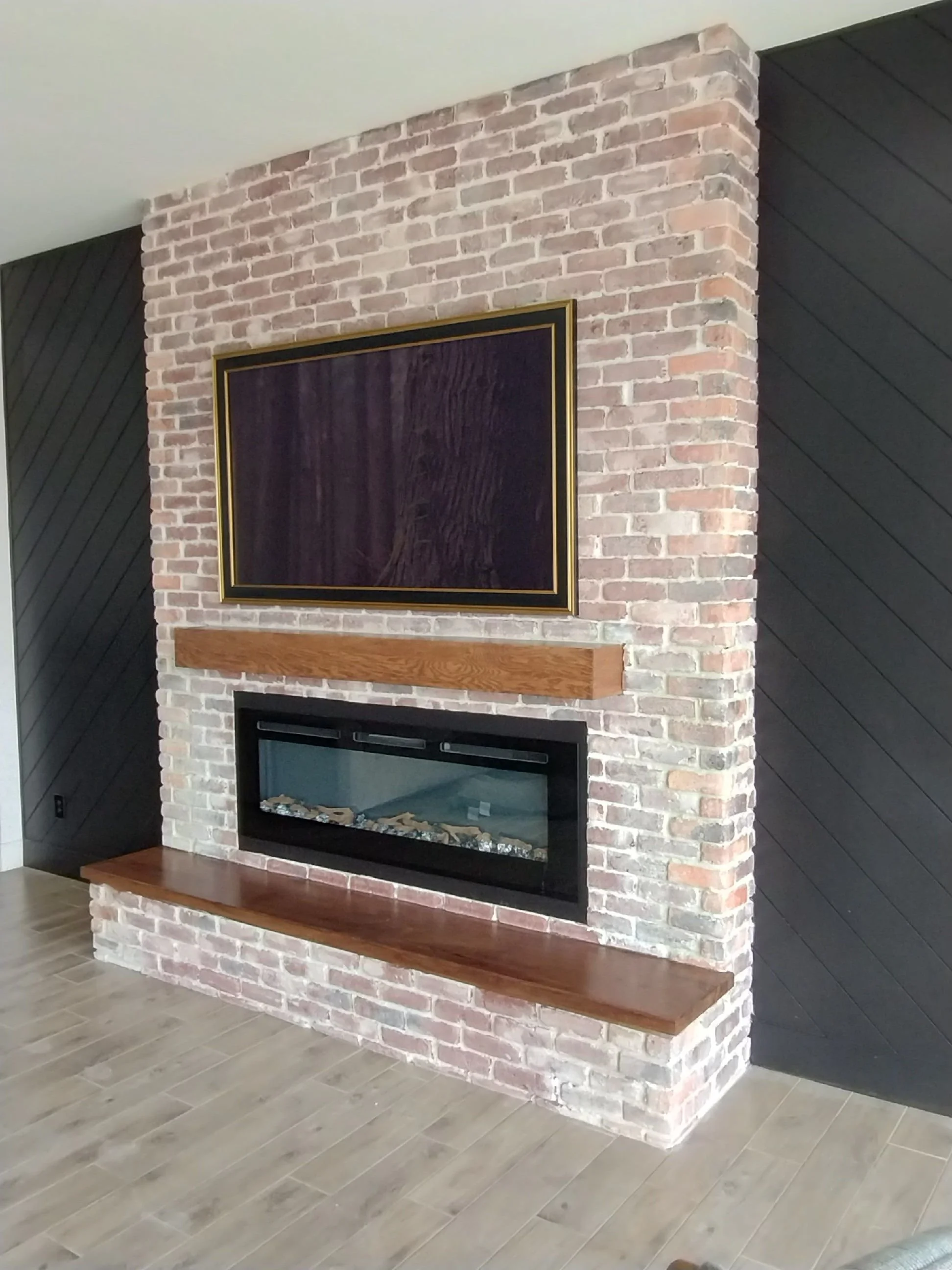 Brick fireplace wall with a wood mantel and dark diagonal side-wall detail