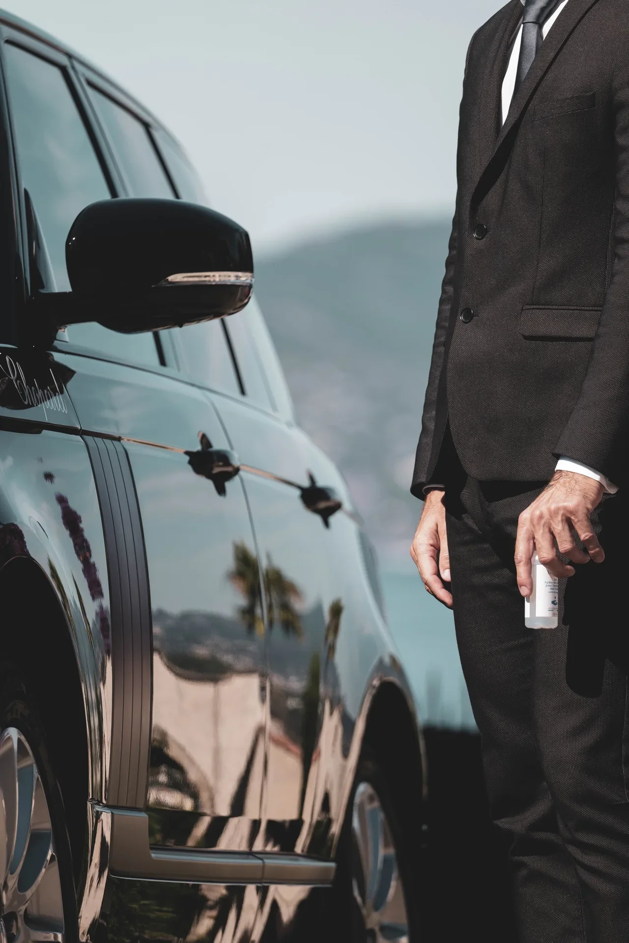 Un chauffeur attend près d’un van, une bouteille d’eau à la main.