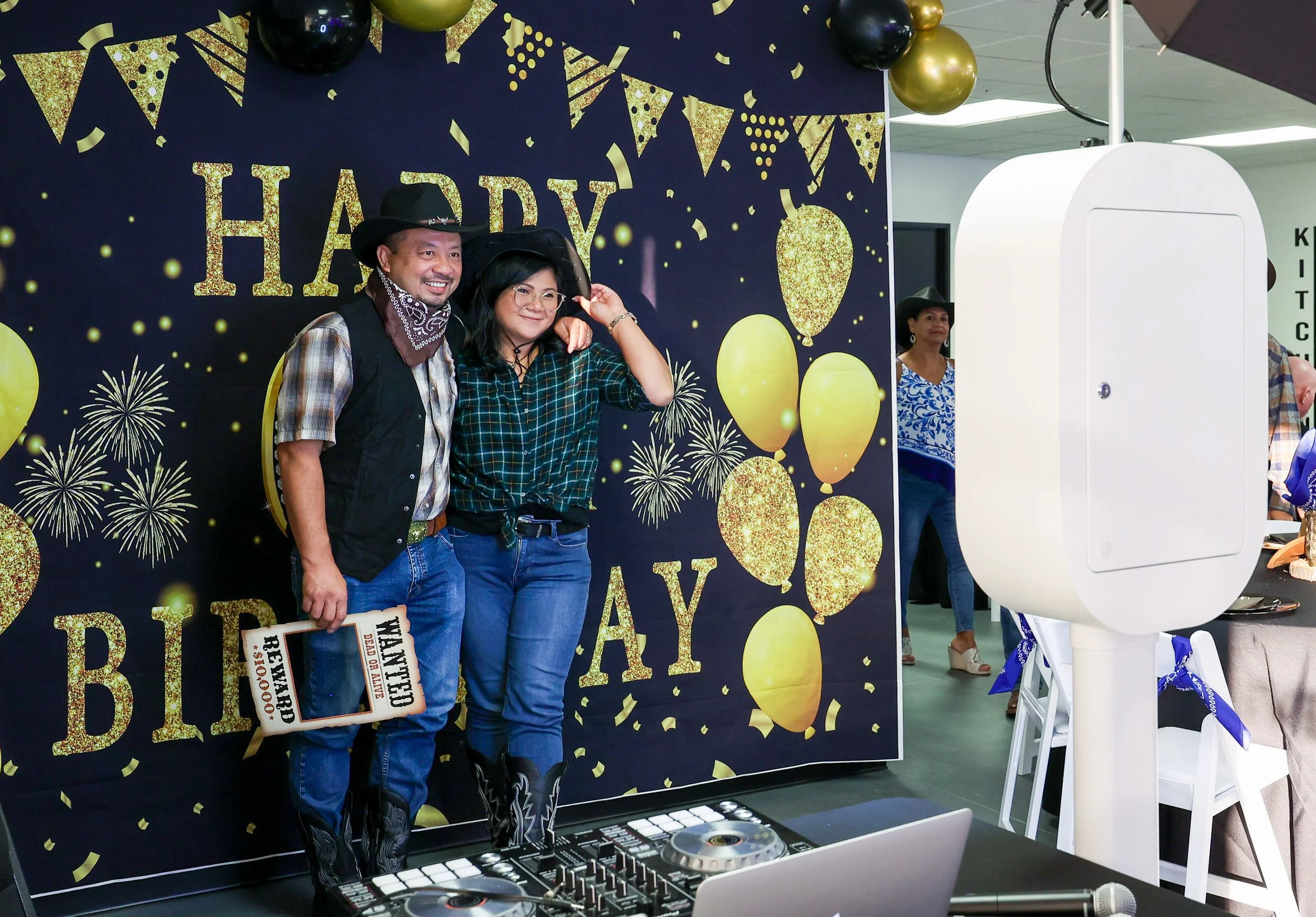 Couple in cowboy hats posing beside the open-air booth at a western-themed birthday