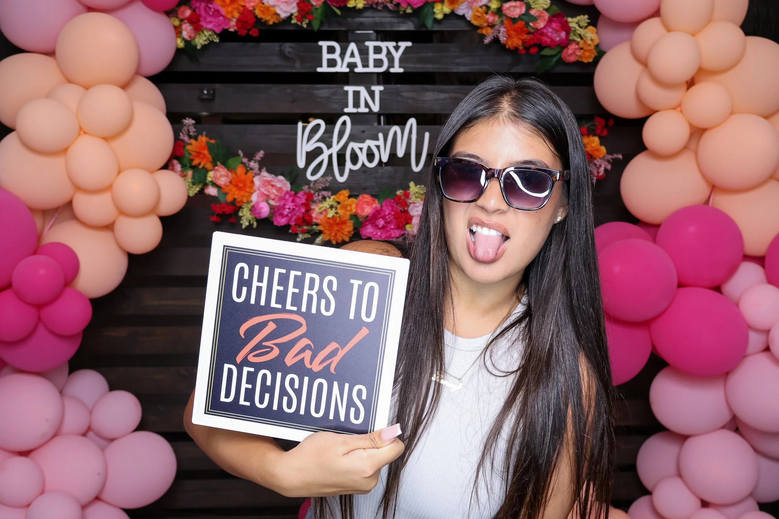 A guest holds a playful sign at the Baby in Bloom photo booth, with flowers and pink balloons