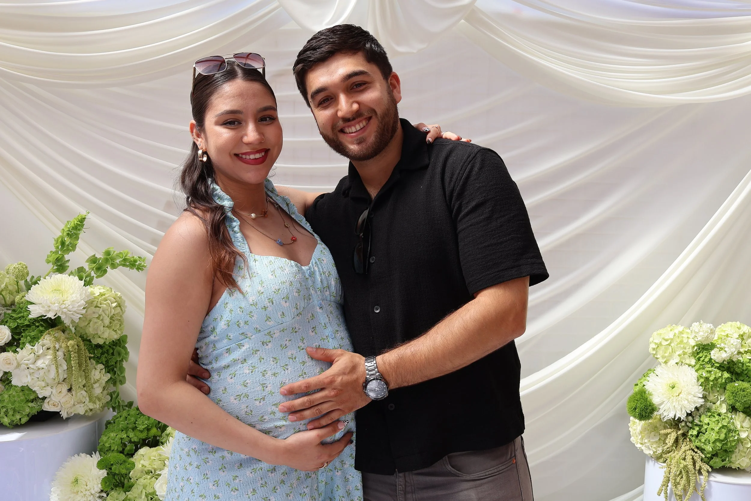 Couple posing in front of a white draped backdrop and floral arrangements