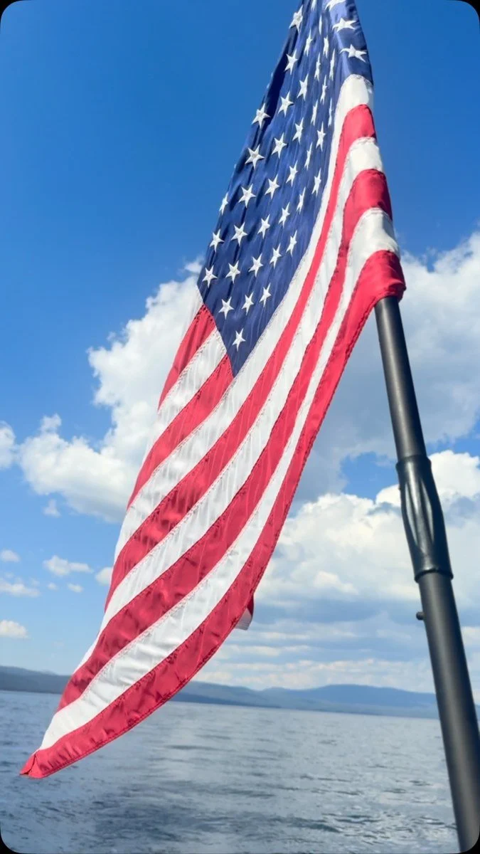 An American flag above Lake Tahoe beneath blue sky and scattered clouds.