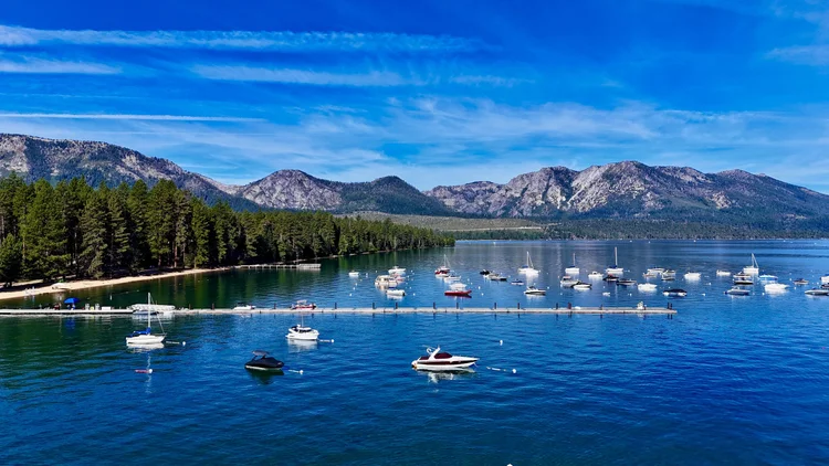 Sailboats and motorboats at a Lake Tahoe marina beneath a broad Sierra mountain ridge.