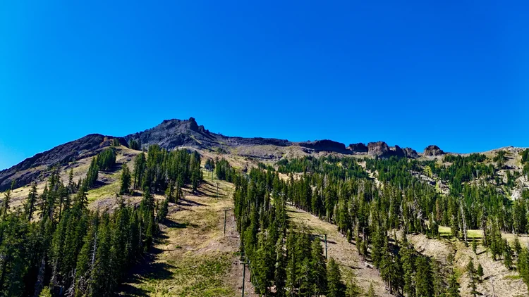 A rocky Sierra ridgeline above summer ski runs, pine trees and chairlift towers.