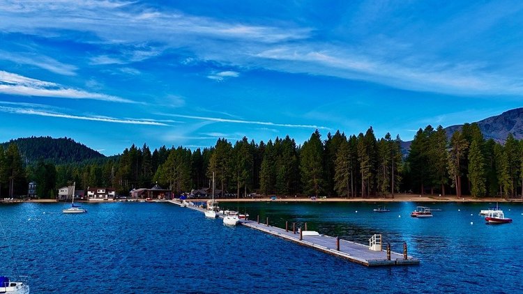Boats beside a long Lake Tahoe marina pier, backed by pine forest and mountains.