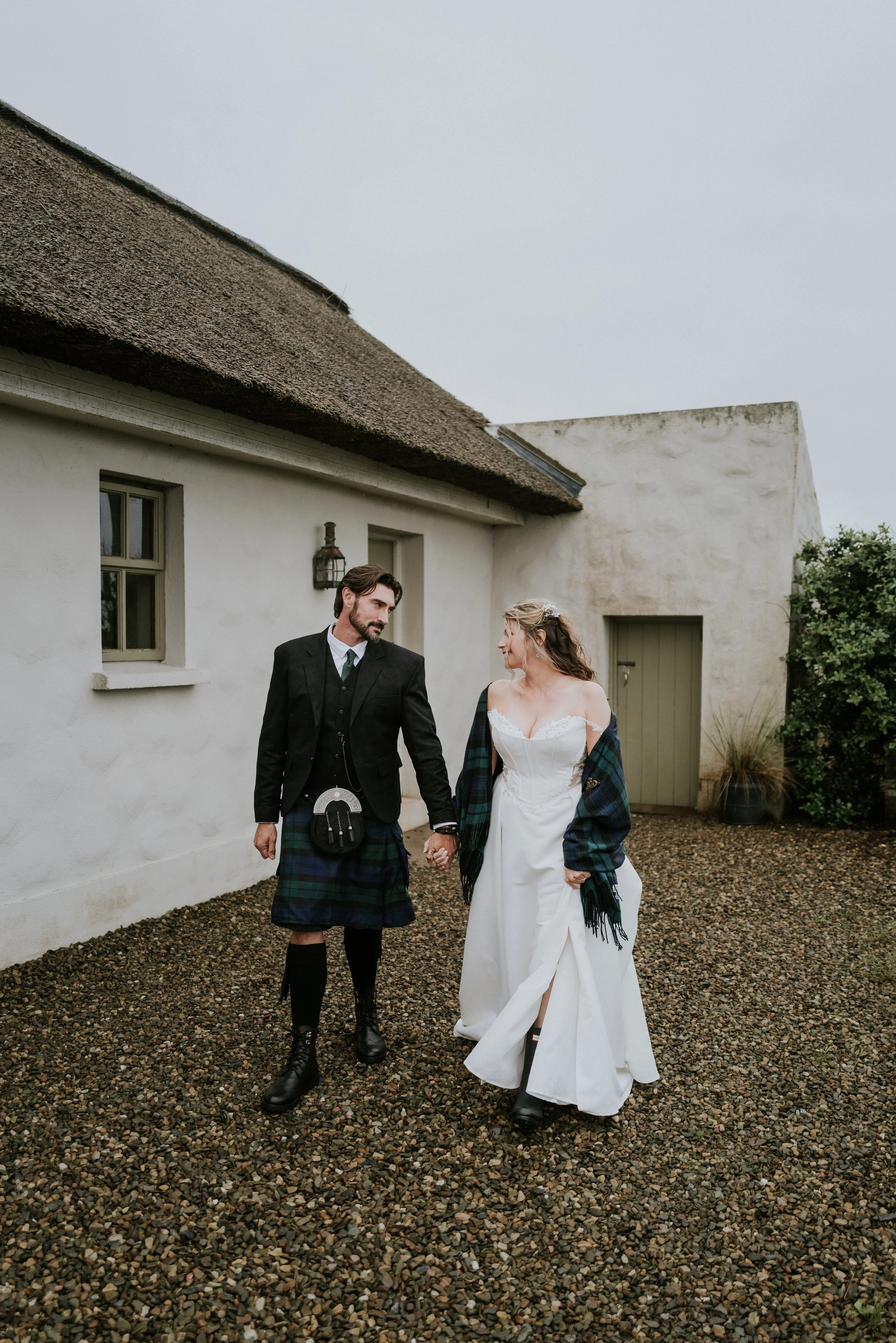 Newly married husband and wife walking outside a beautiful Irish thatched cottage after their elopement ceremony in Ireland