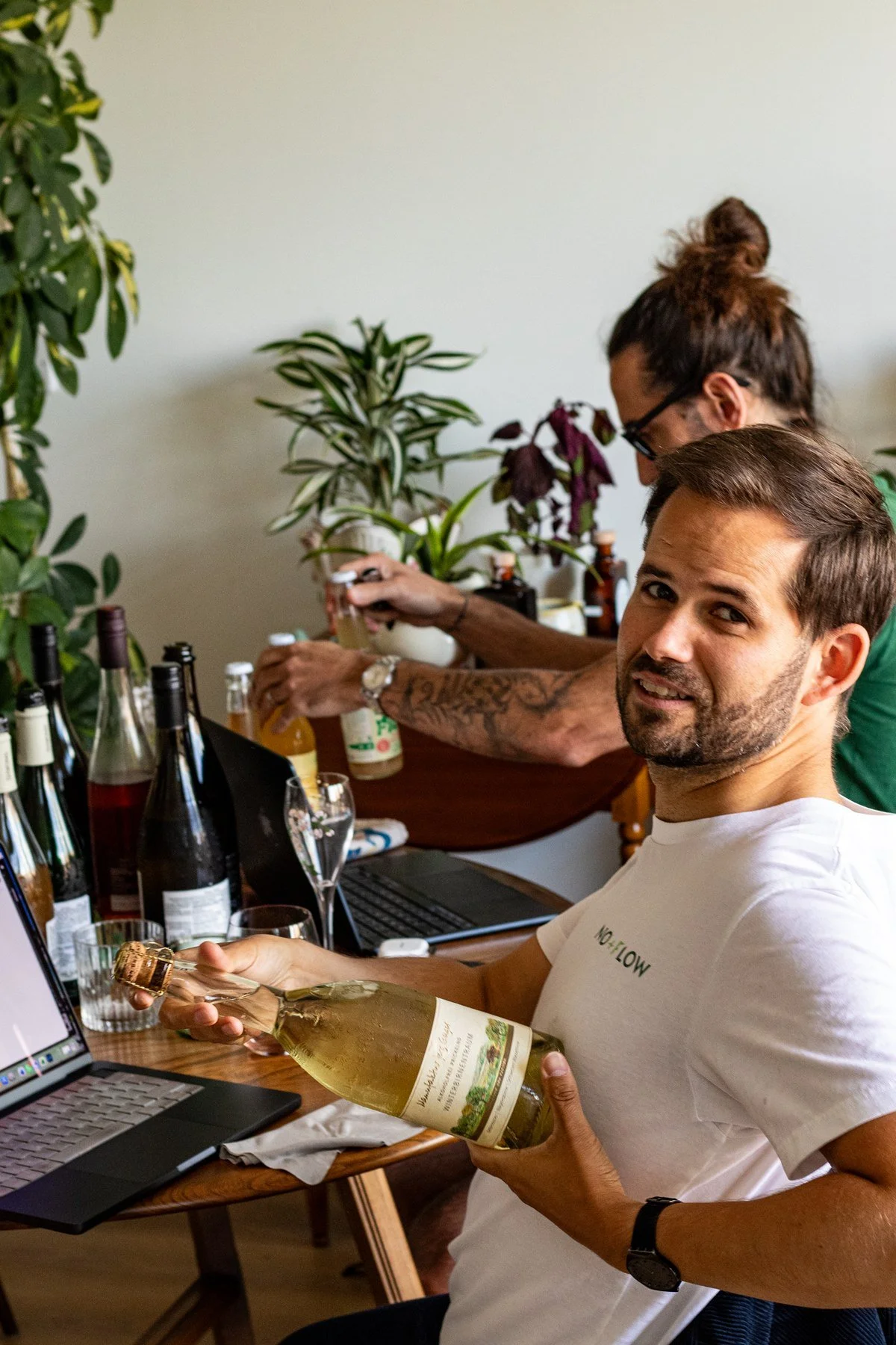 Matthias in a No+Flow t-shirt pouring wine at a team tasting session, with teammates in the background