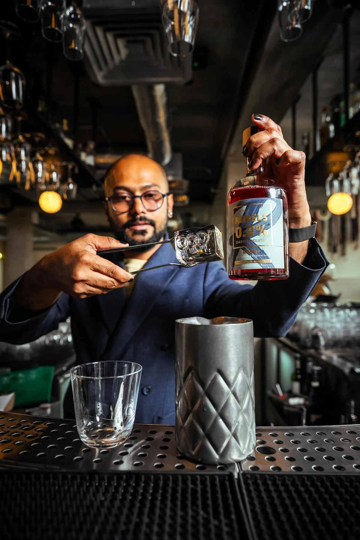 A bartender garnishing a Rebels 0.0% cocktail with ice and tongs behind the bar