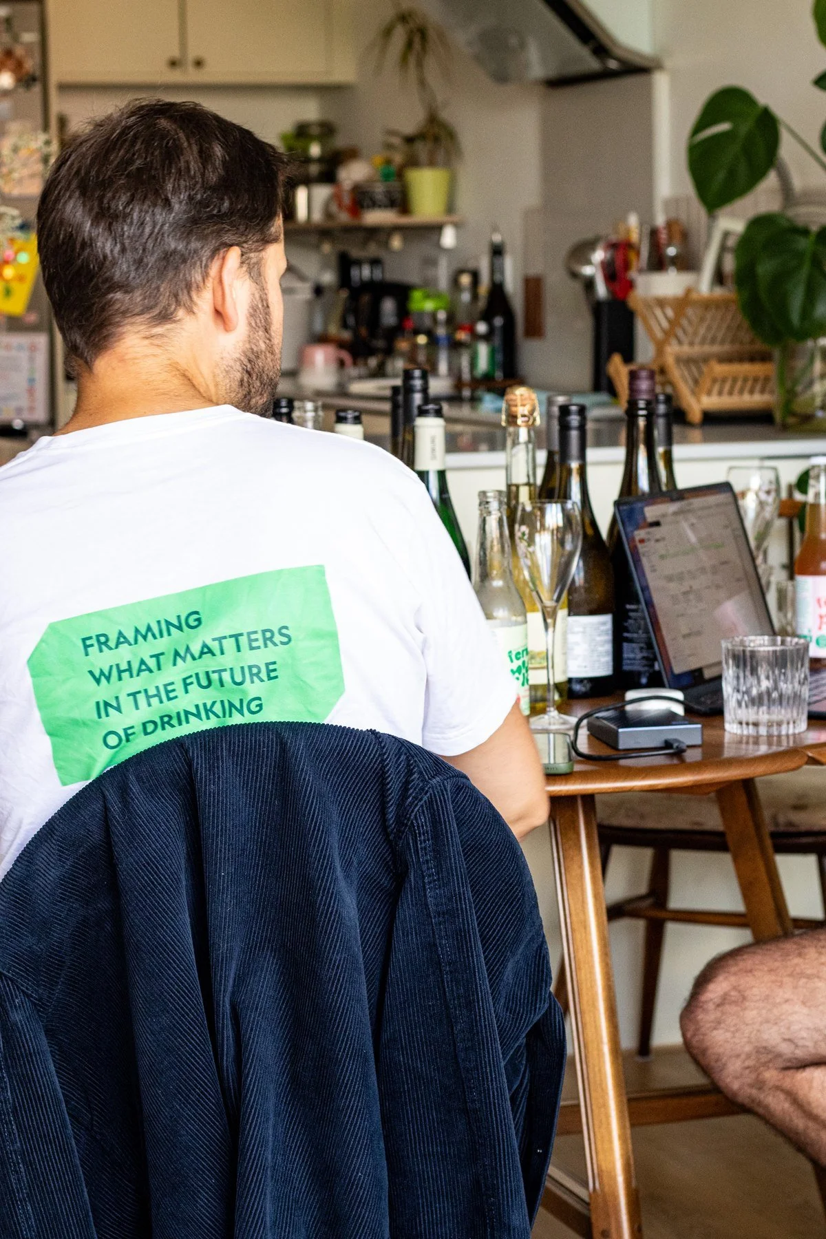 The back of a white t-shirt printed with the No+Flow tagline, Framing what matters in the future of drinking, worn at a home tasting session