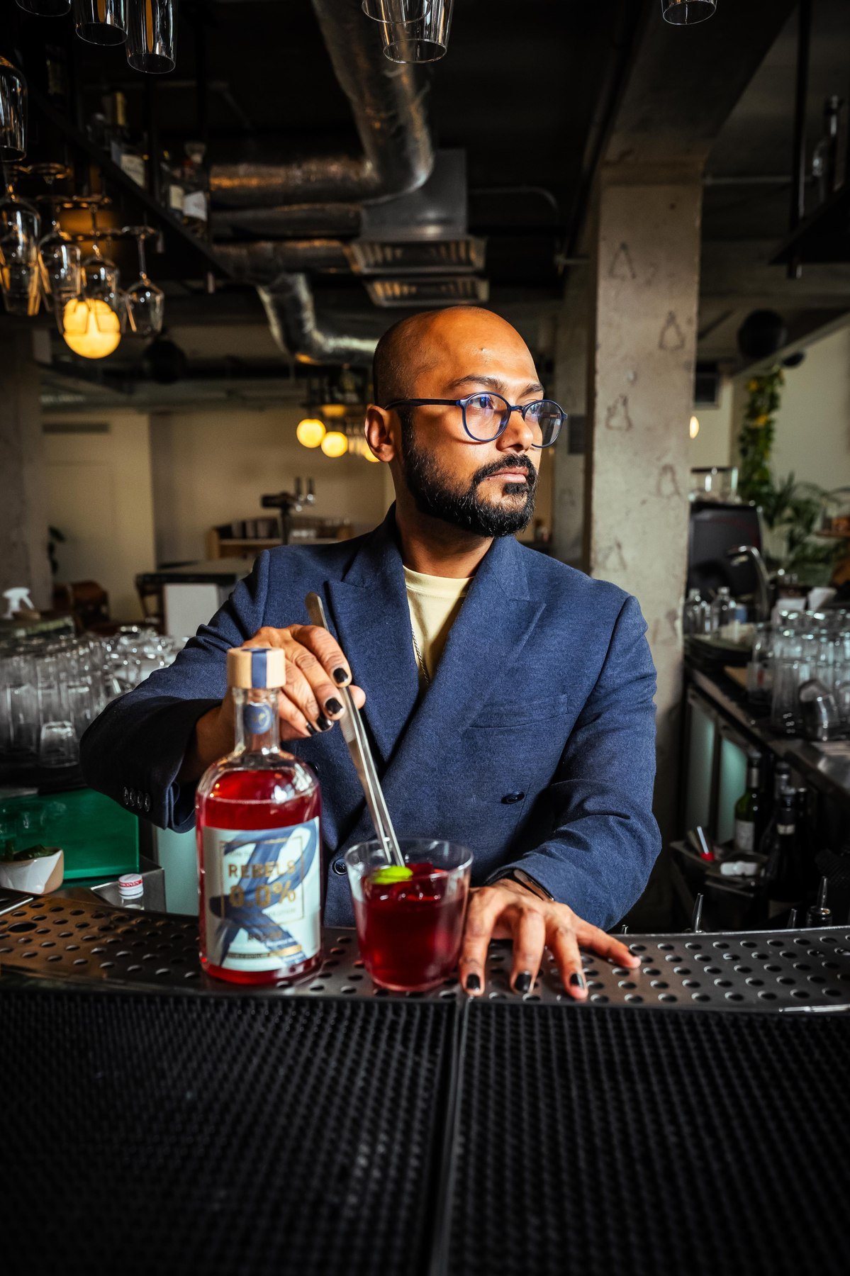 A bartender behind the bar with a bottle of Rebels 0.0% and a finished cocktail