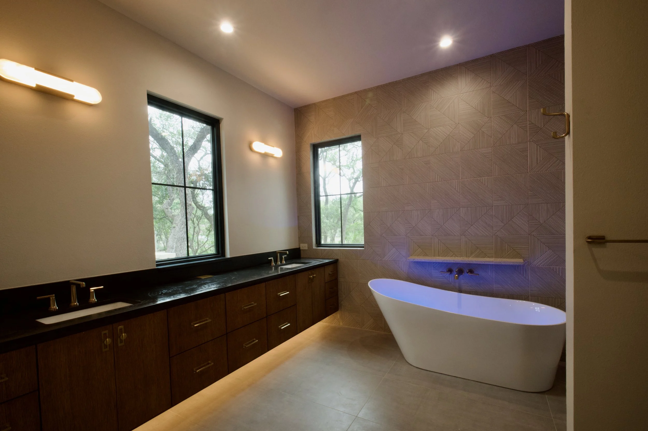 Primary bathroom white oak vanity finished with Broadway Black Leathered quartz, soaking tub visible beyond