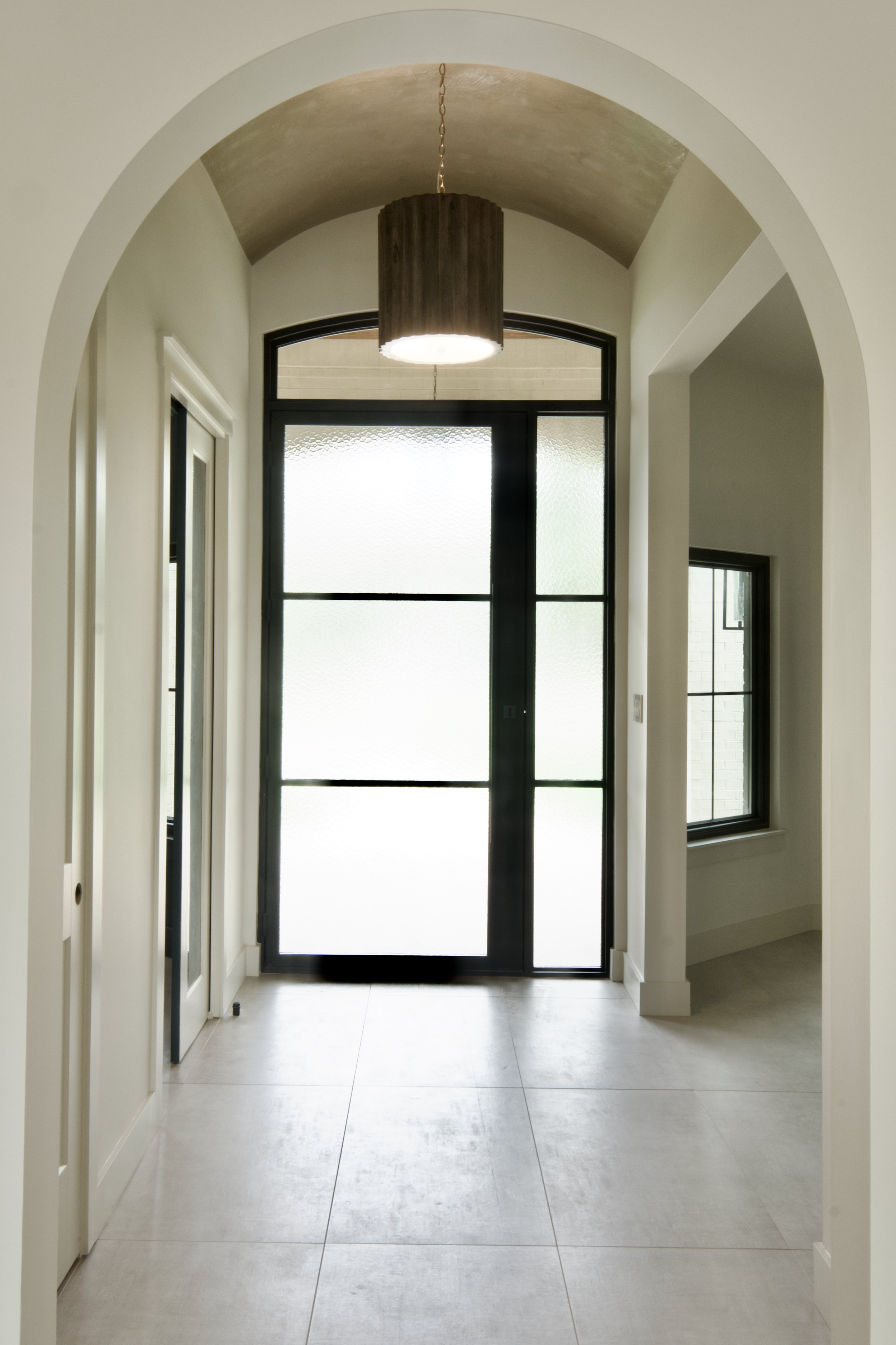 Custom black iron pivot entry door with transom and sidelights set within a barrel-vault arch, 10 feet 7 inches tall