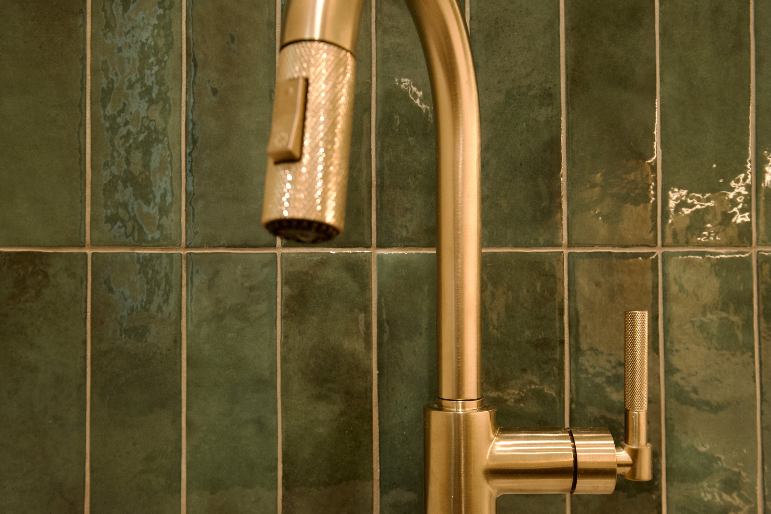 Detail of brushed gold faucet against green tile in the butler's pantry