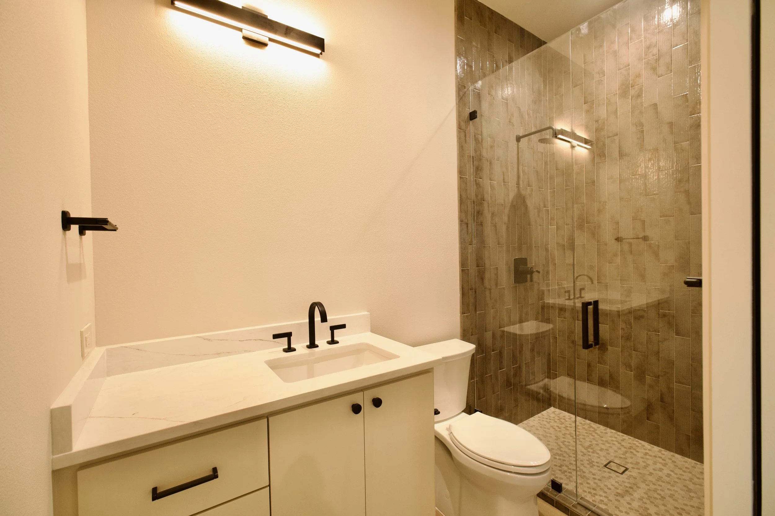 Renovated guest suite bathroom with vanity, glass shower, and wood-look tile