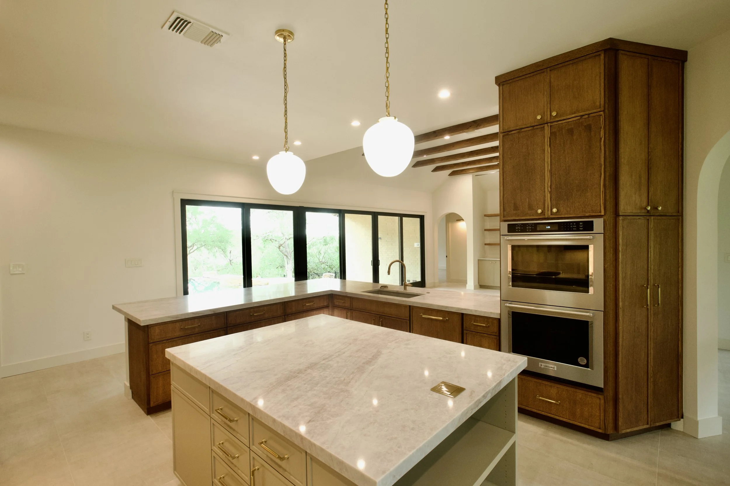 Full kitchen view with island, pendants, white oak cabinetry, and stained beams