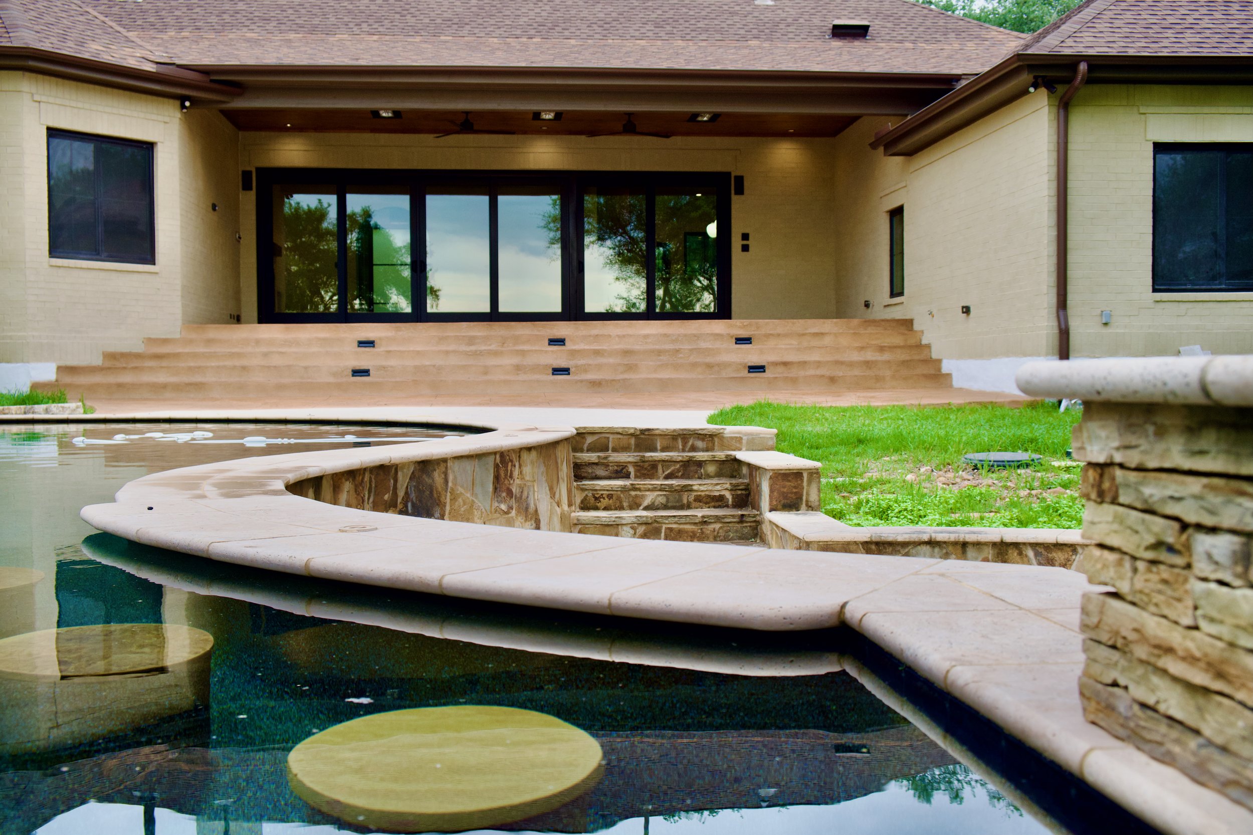 Elevated patio with stained tongue-and-groove ceiling, stone steps, and pool view