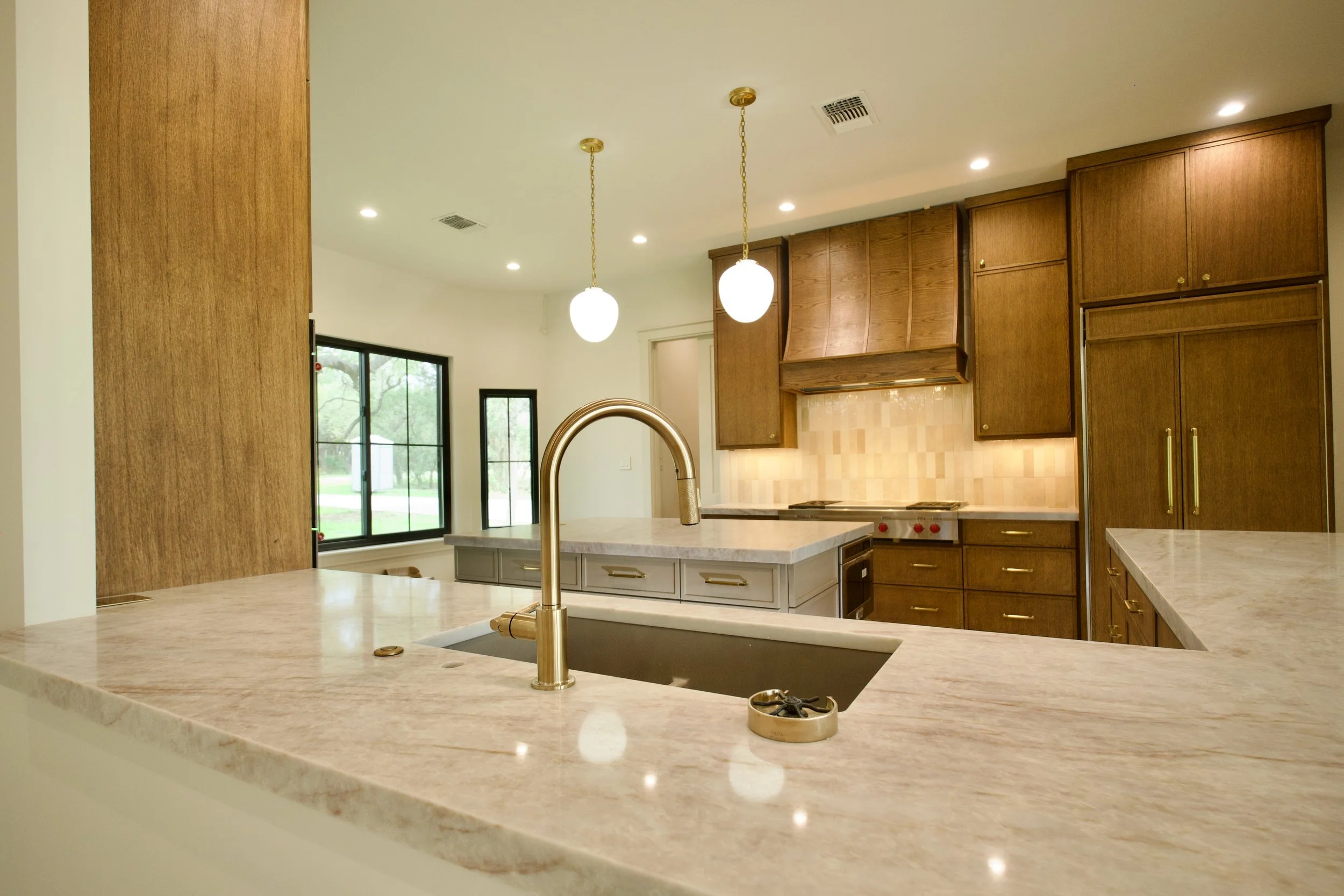 Custom kitchen with mitered Perla Mirage quartz island, Wolf cooktop, custom vent hood, and white oak cabinetry