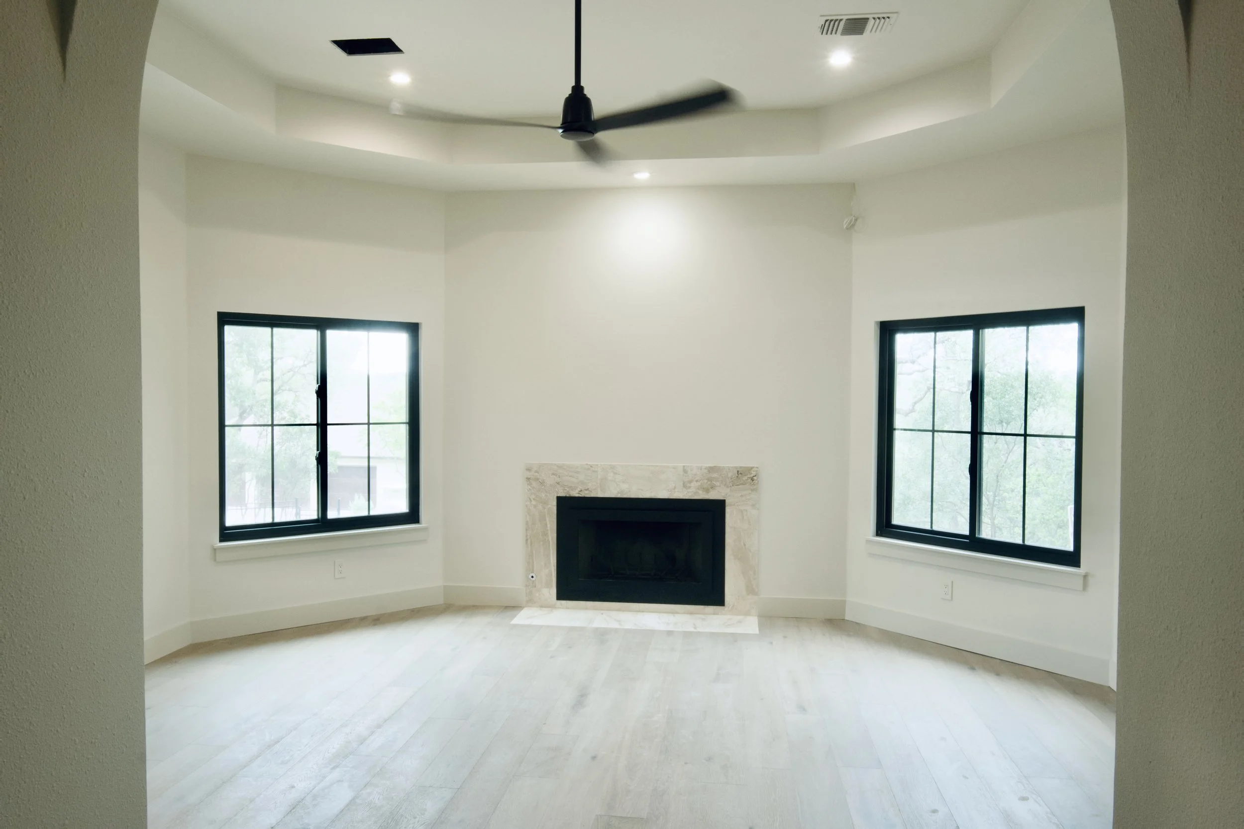 Primary bedroom symmetric view featuring the fireplace, ceiling fan, and black-trimmed windows