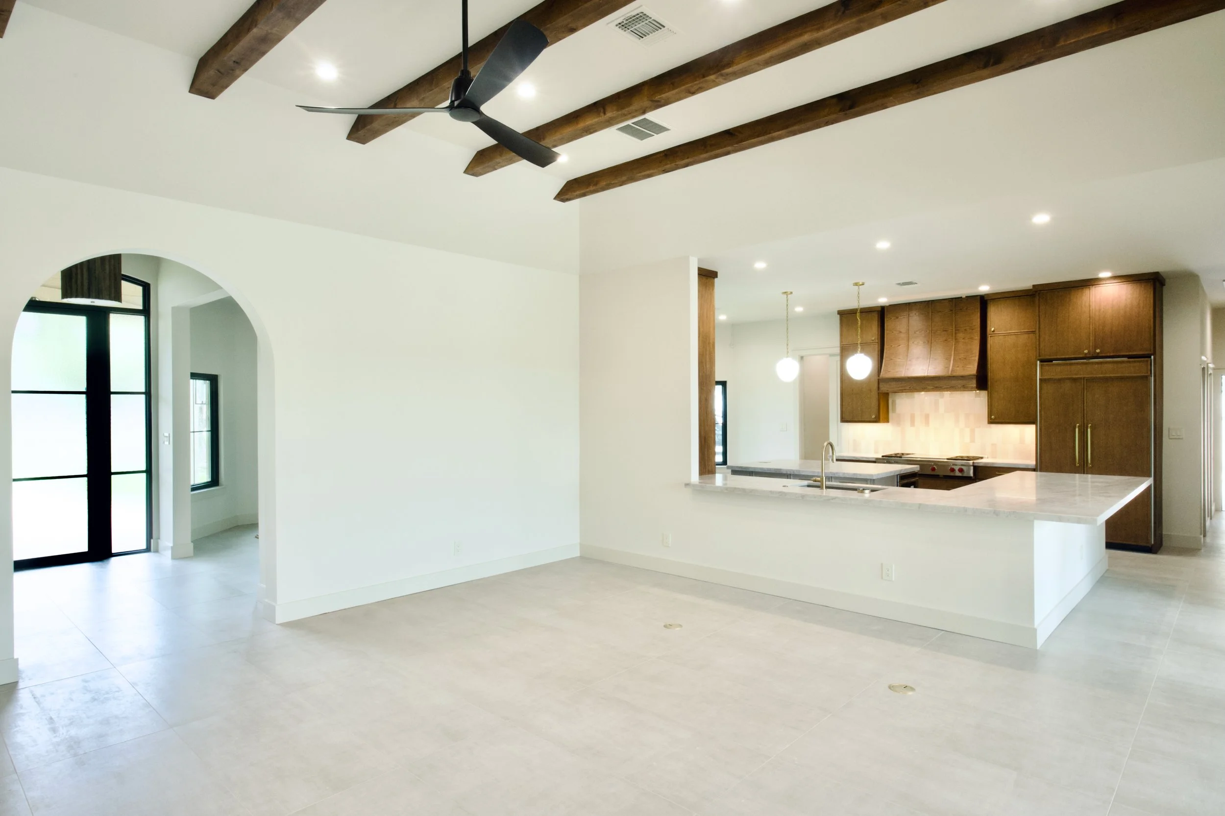 Open-concept living area with stained beams flowing into the kitchen, finished with Fray Sand porcelain flooring