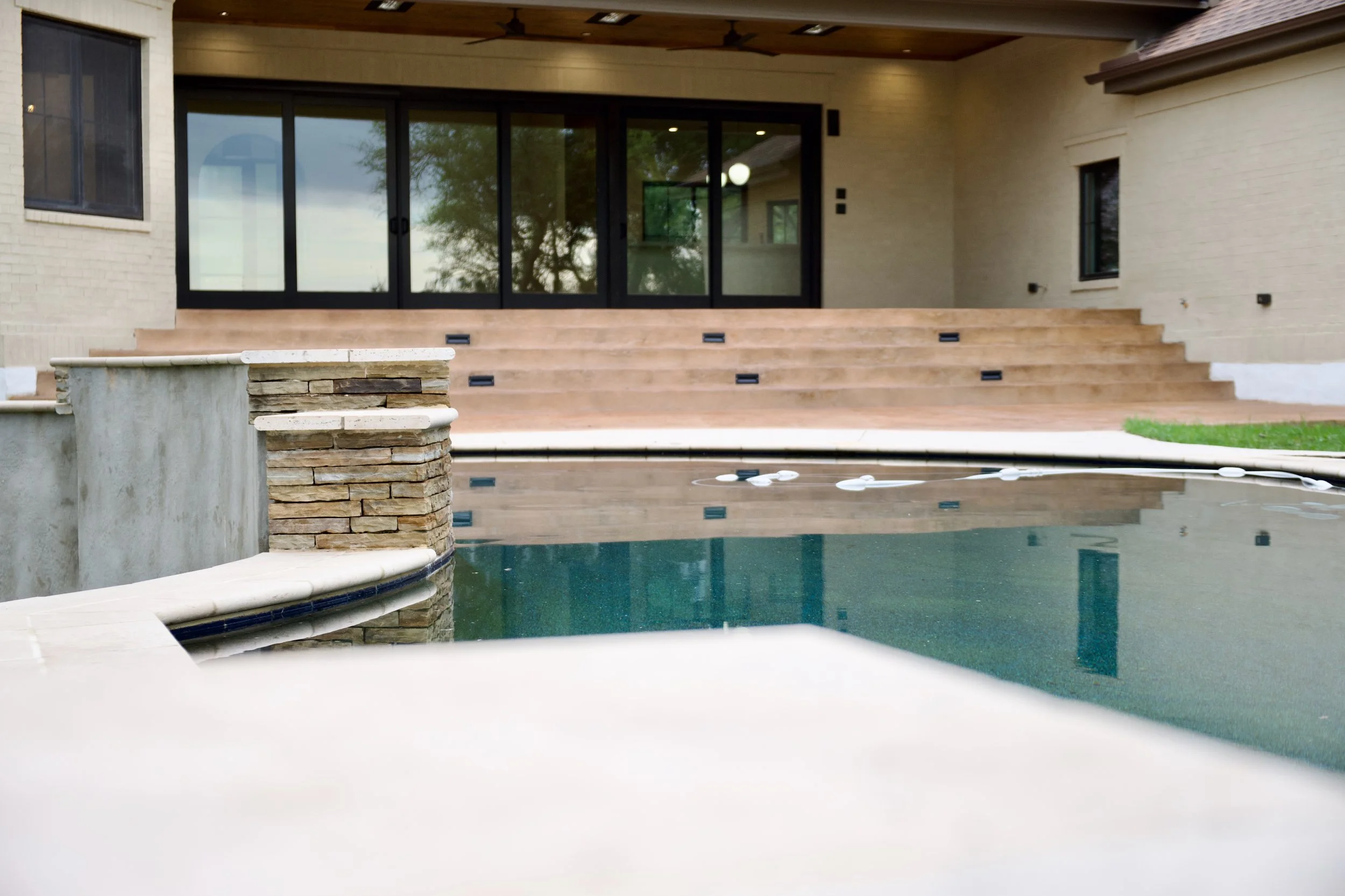 Rear elevation of the San Marcos whole-home renovation showing lime-washed brick, black Andersen sliding doors, covered patio, and pool by Riverbend Hill Country Homes