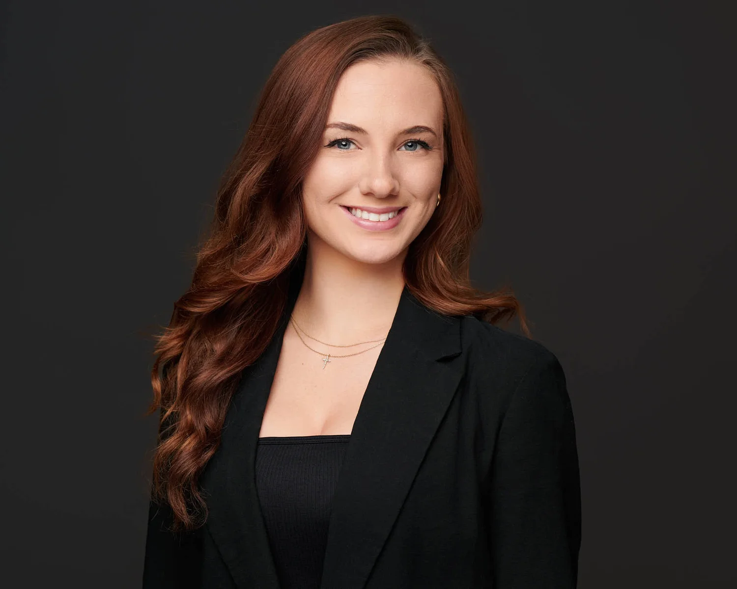 Color headshot of a woman in a black blazer on a dark ground, photographed by Ryan Dunbar